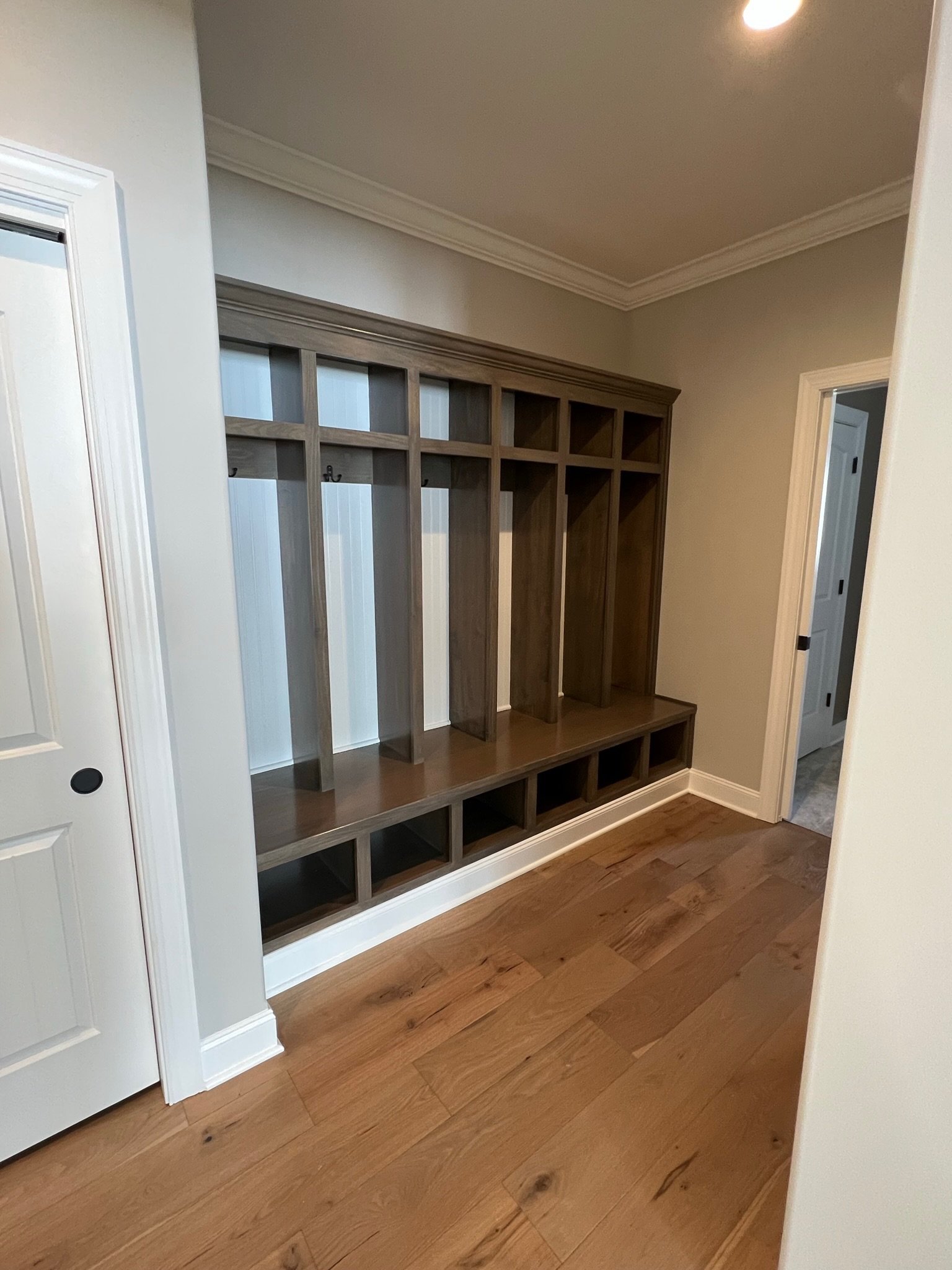 Wooden mudroom bench with cubbies and coat hooks in a hallway.