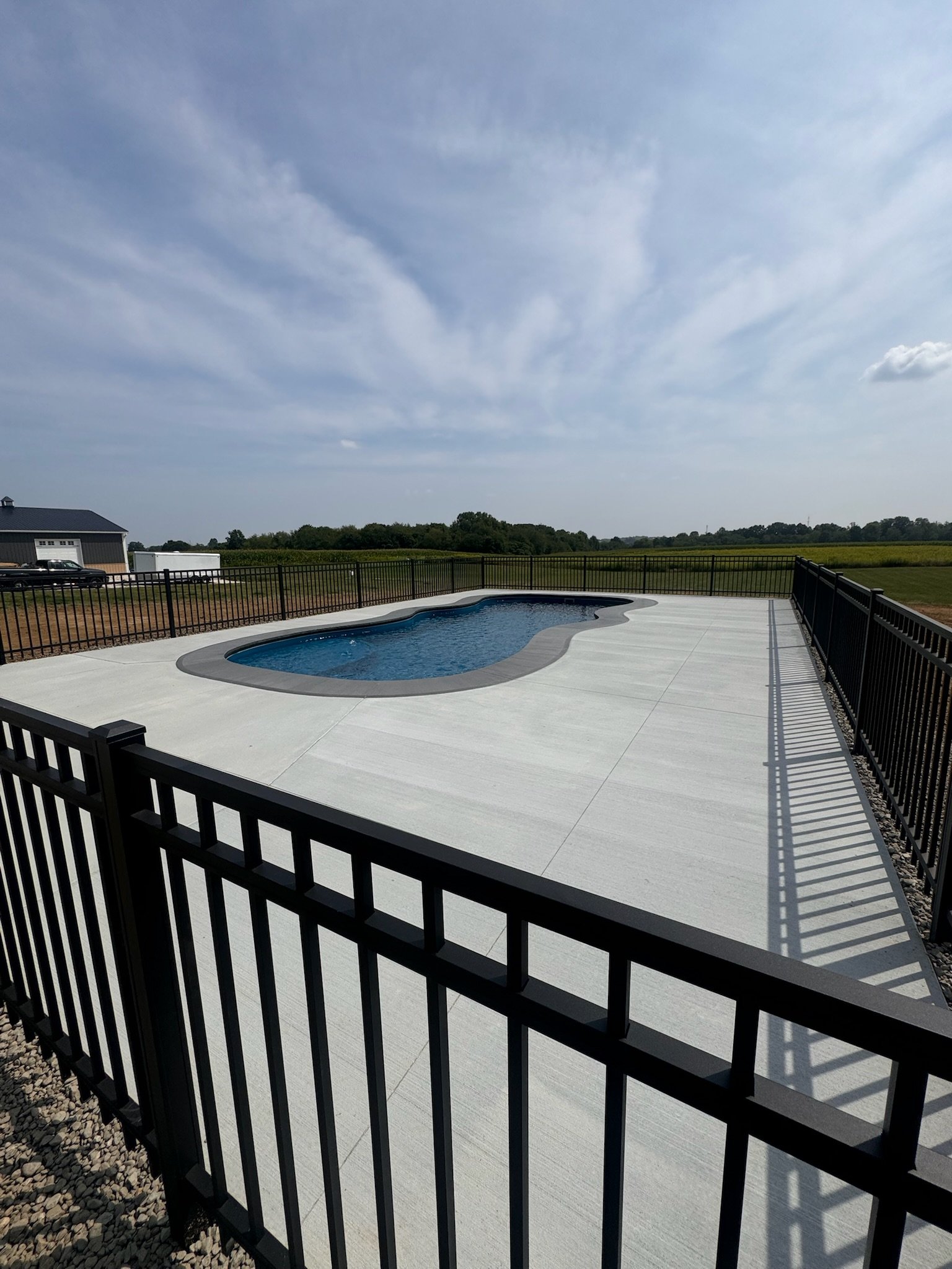 Swimming pool with surrounding metal fence, concrete deck, and open countryside.