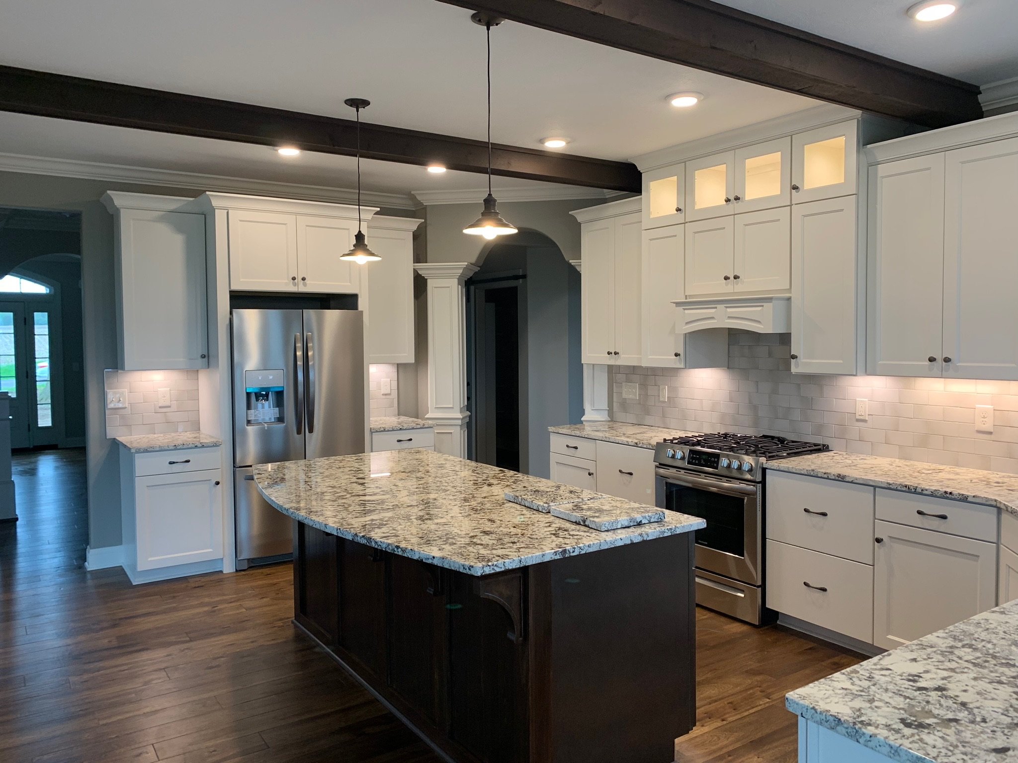 Modern kitchen with white cabinets, granite countertops, stainless steel appliances, and pendant lighting. Features a central island, wooden floor, and recessed ceiling lights.
