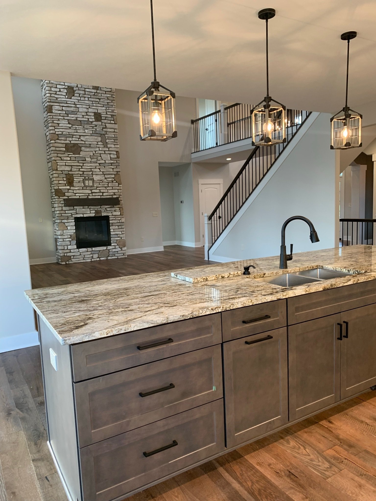 Modern kitchen with stone fireplace, island with marble countertop, pendant lights, and wooden floors.