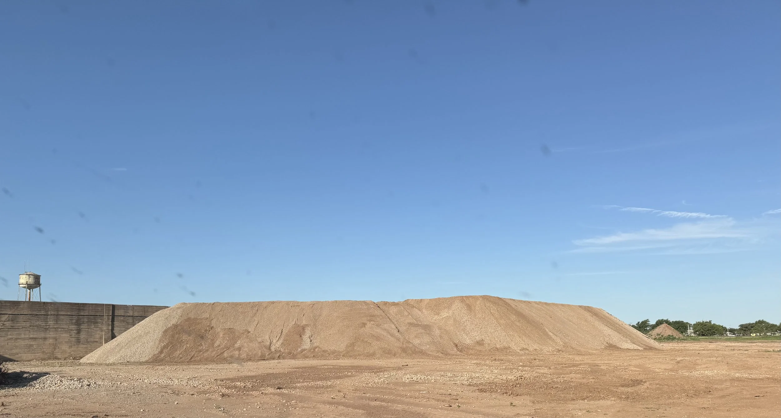 Large piles of crushed concrete at crushing site. A water tower is visible in the background.