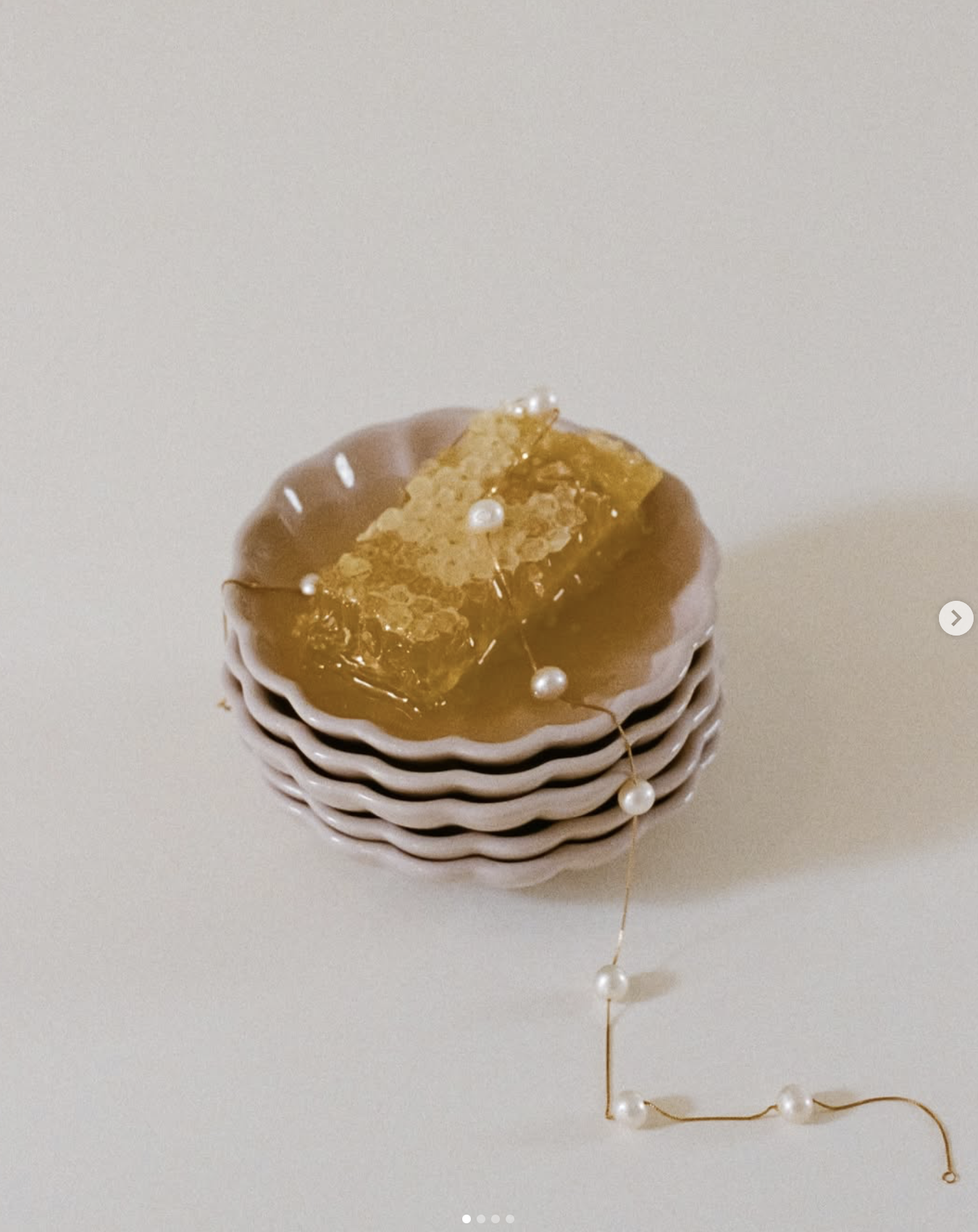Stack of pink bowls with honeycomb on top of a white surface, decorated with a string of pearls.