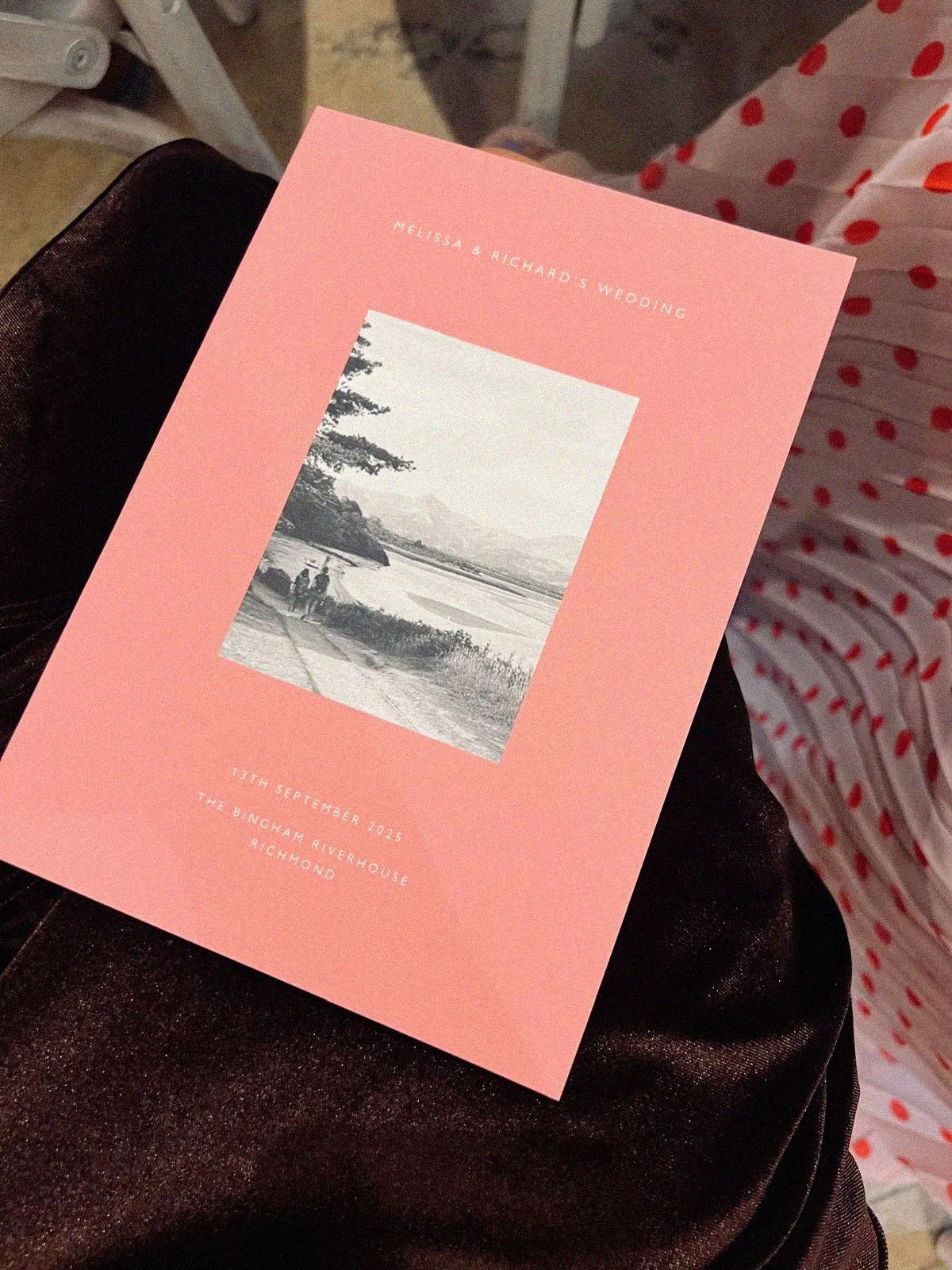 Pink wedding invitation card with black and white landscape photo, text about Melissa and Richard's wedding, date September 13, 2023, at The Bingham Riverhouse in Richmond.