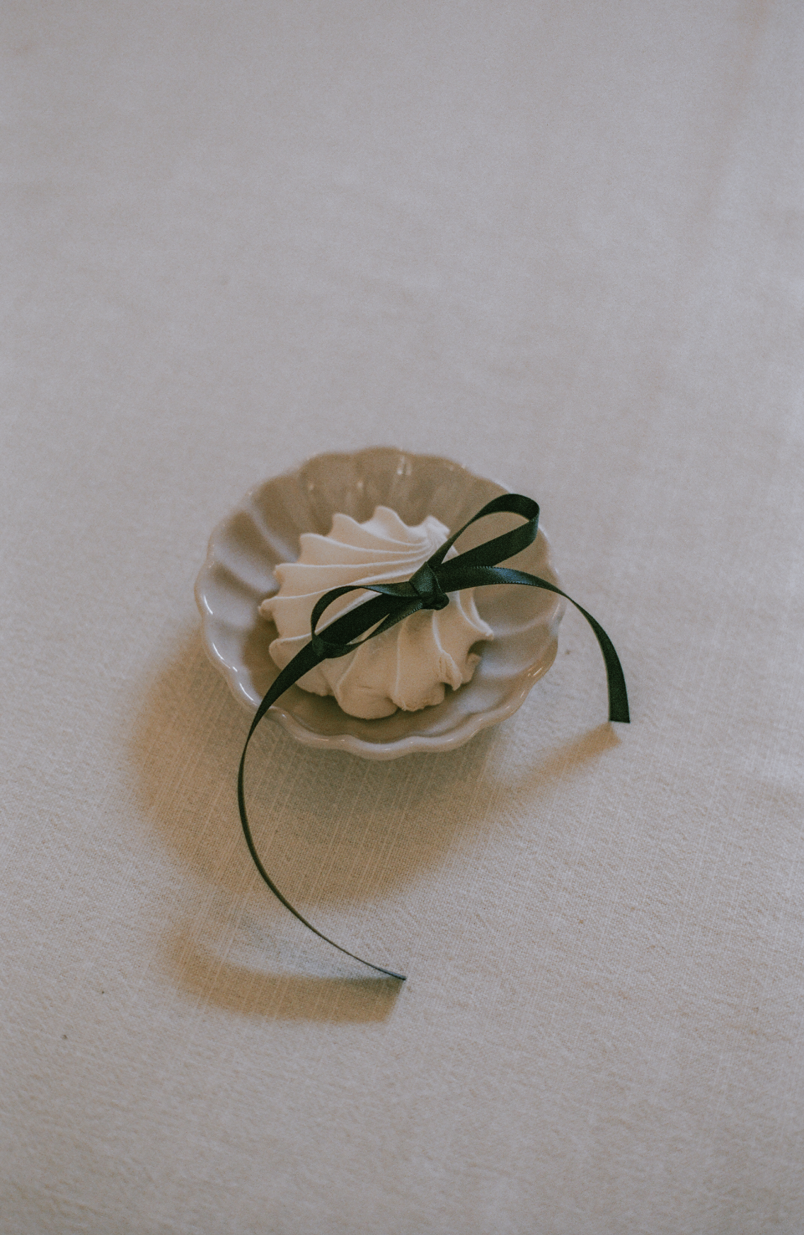 Cream-colored pastry with a dark green ribbon in a small white scalloped dish on a beige tablecloth.