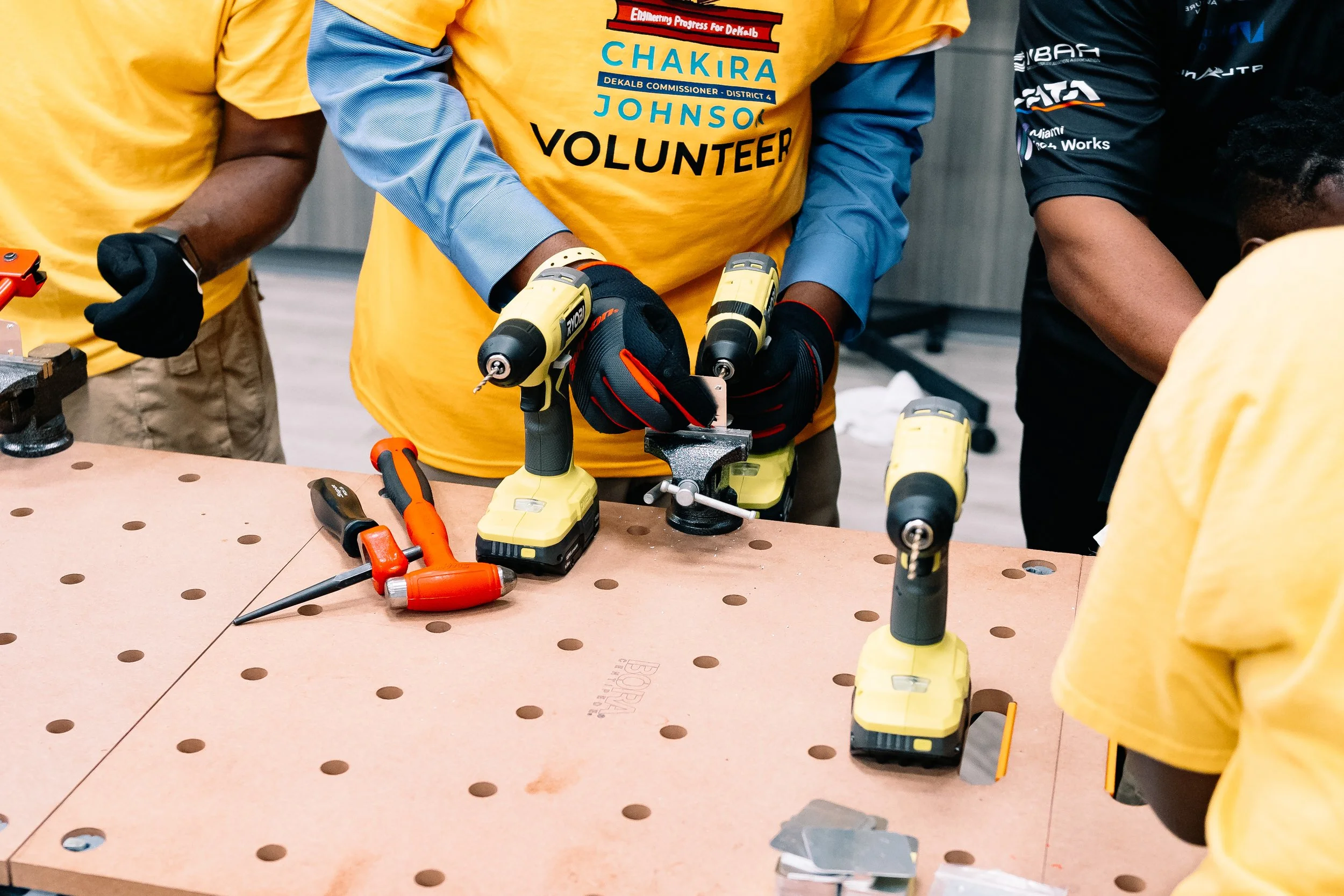 Chakira’s Cookout volunteer uses a cordless drill at a tool-equipped workstation during a hands-on building activity led by BITTS.