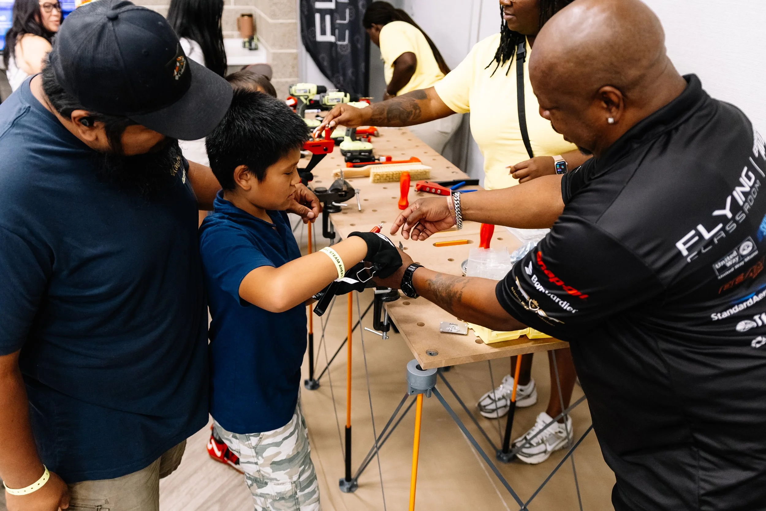 A BITTS instructor assists a young attendee with a hands-on building project as another adult looks on during Chakira’s Cookout.