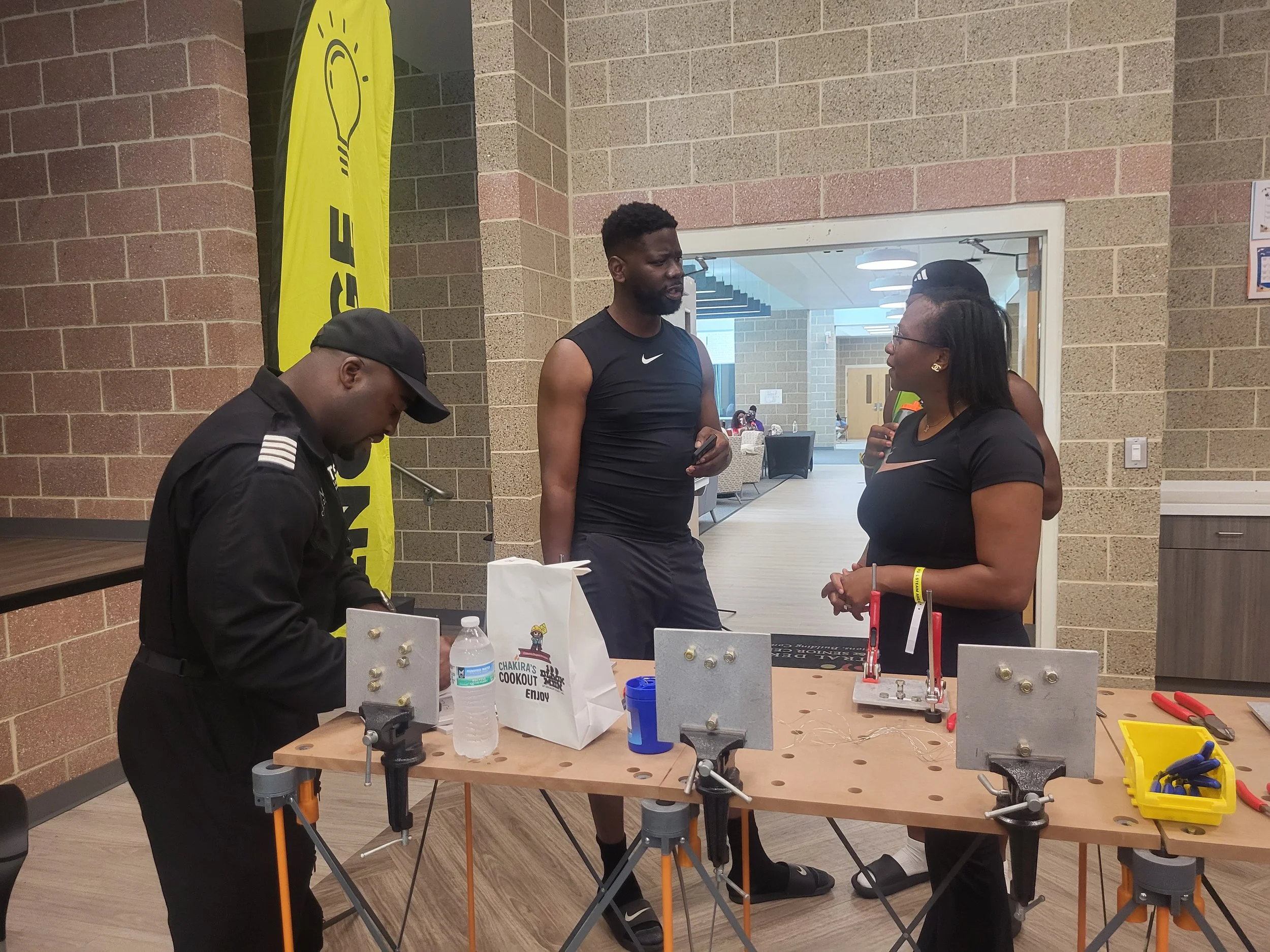 Aviation pioneer and Flying Classroom founder Captain Barrington Irving works at a hands-on engineering station equipped with vises and tools while attendees gather nearby.