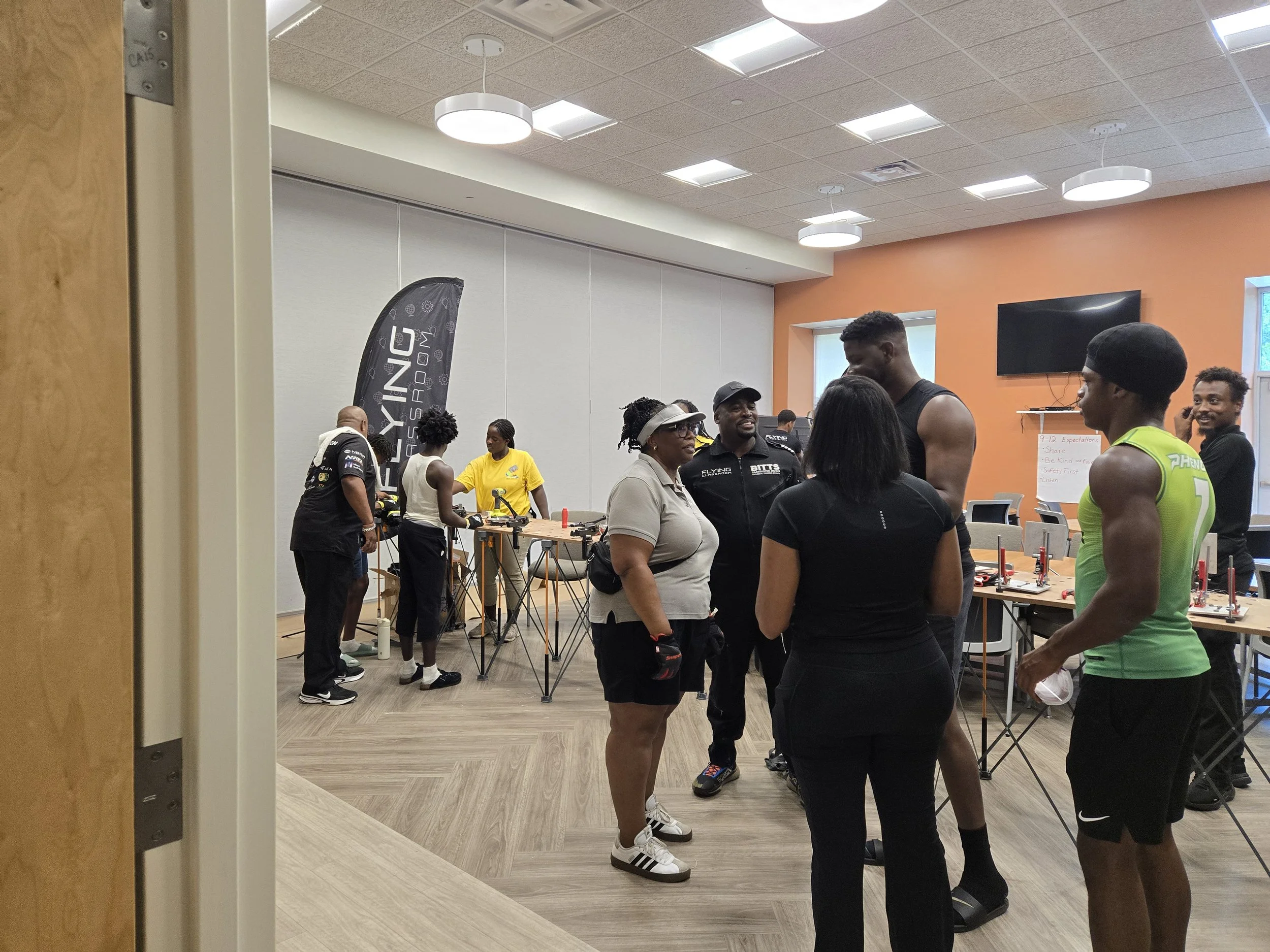 Commissioner Chakira Johnson talks with a group beside tool-equipped activity tables while participants work at STEAM stations in the background.