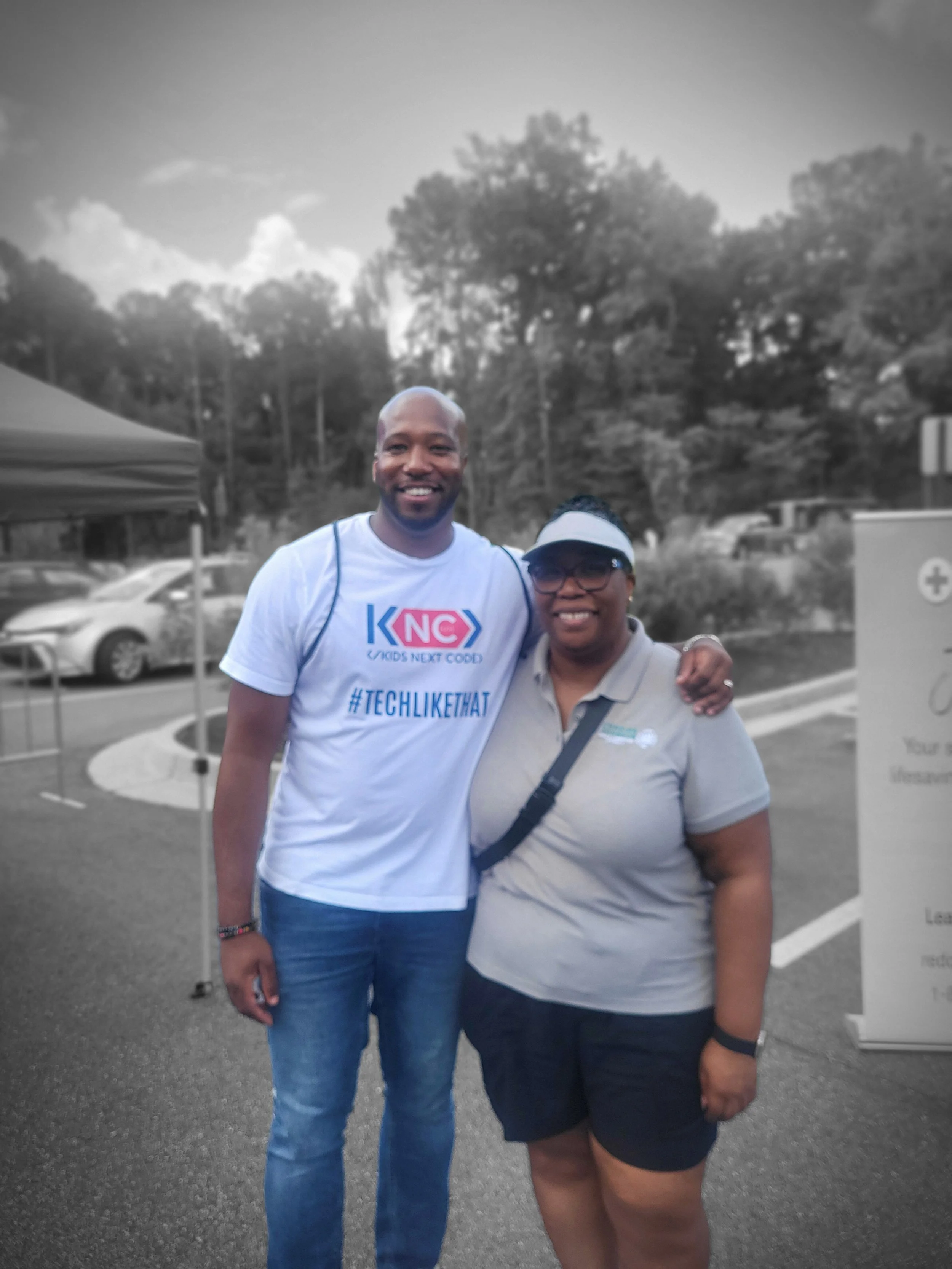 Kids Next Code Founder and Director Travis Reeves and Commissioner Chakira Johnson smile and pose side by side outdoors at Chakira’s Cookout.
