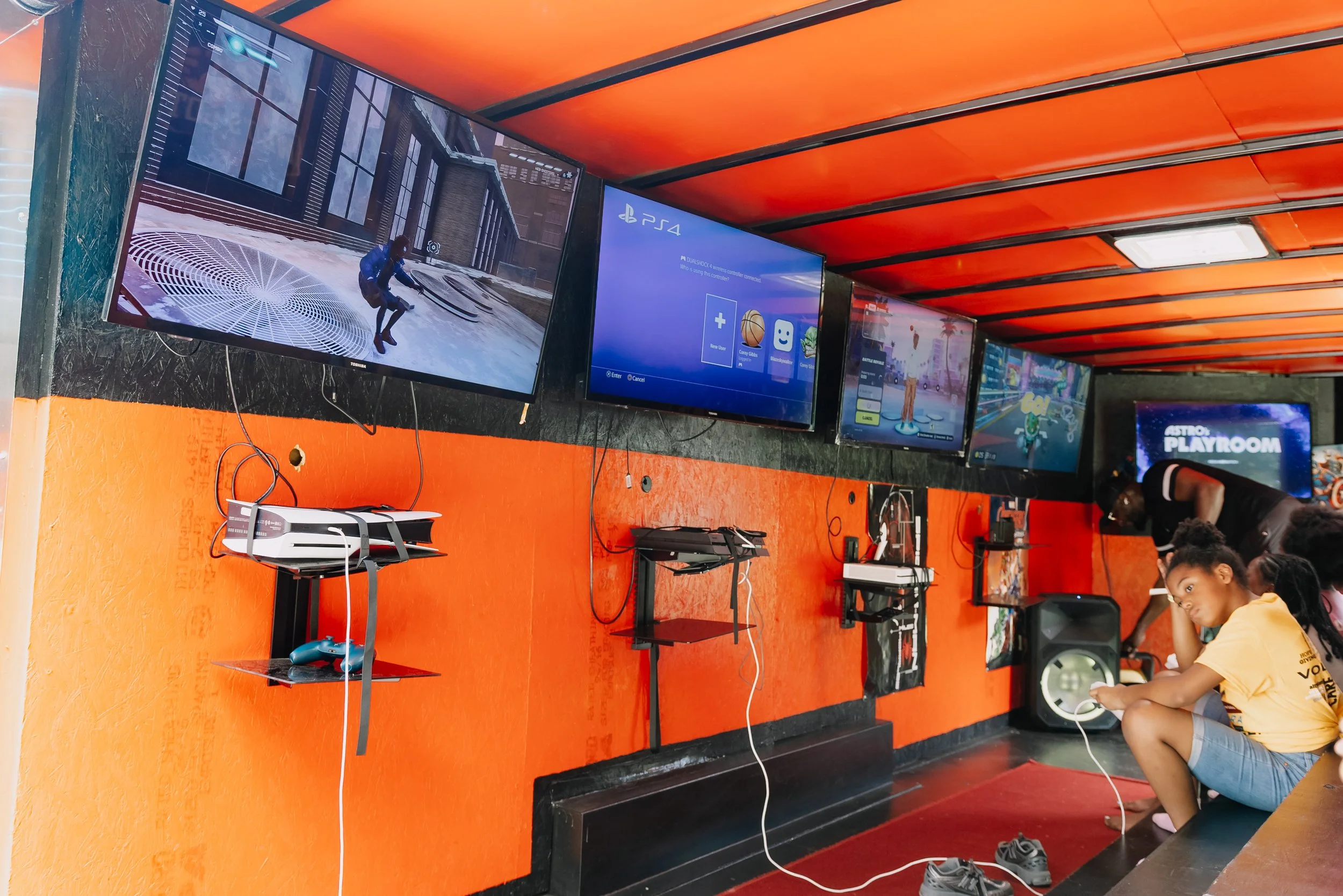 Inside a mobile gaming bus at Chakira’s Cookout, multiple screens and video game consoles are set up for children to play.