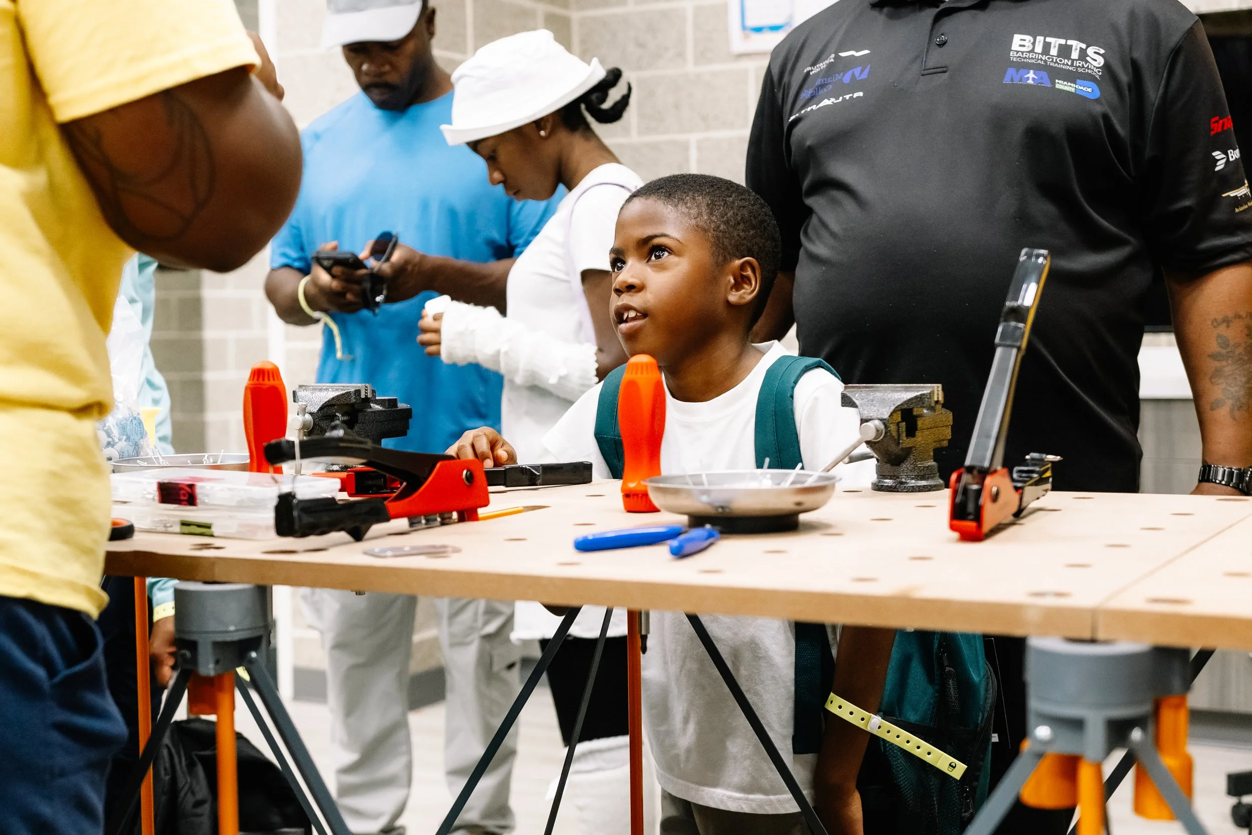 Young attendee listens to instructions at a tool-equipped workstation during a hands-on building activity led by BITTS at Chakira’s Cookout.