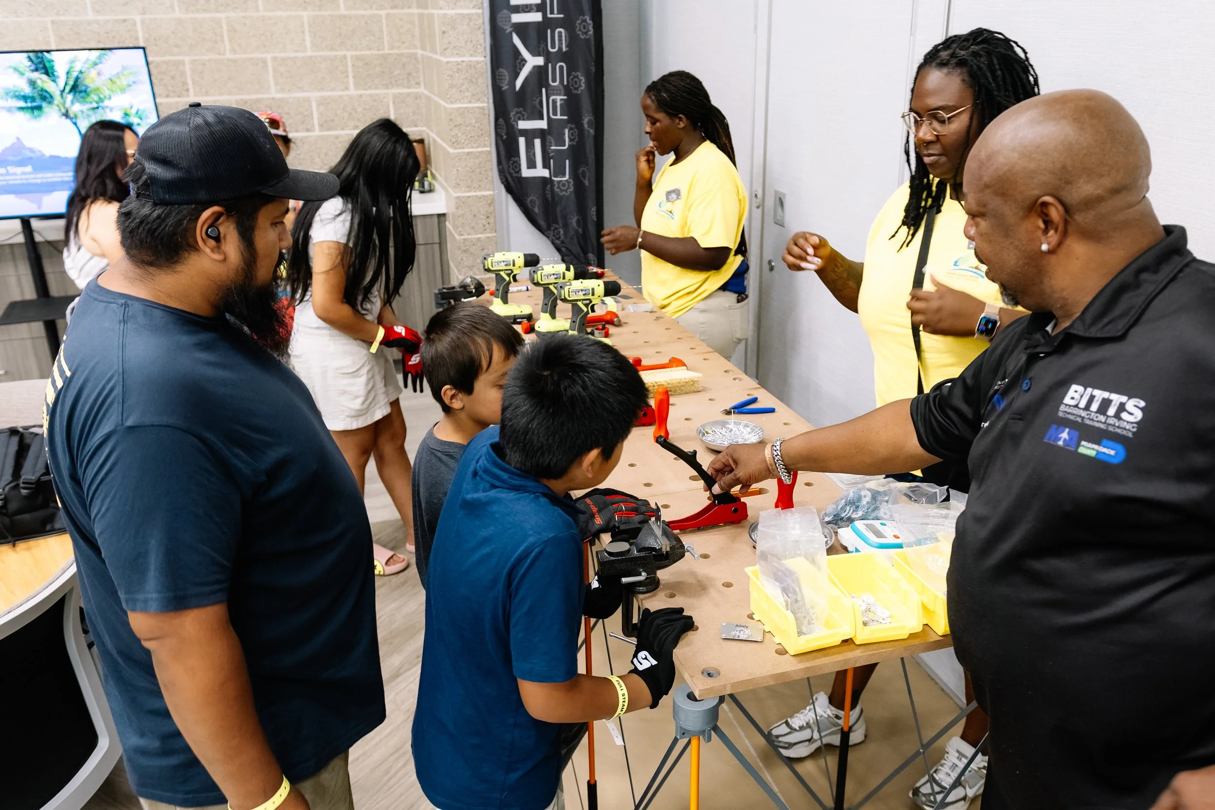 Children participate in a hands-on building activity with guidance from BITTS instructors and Chakira’s Cookout volunteers at a workstation filled with tools and materials.