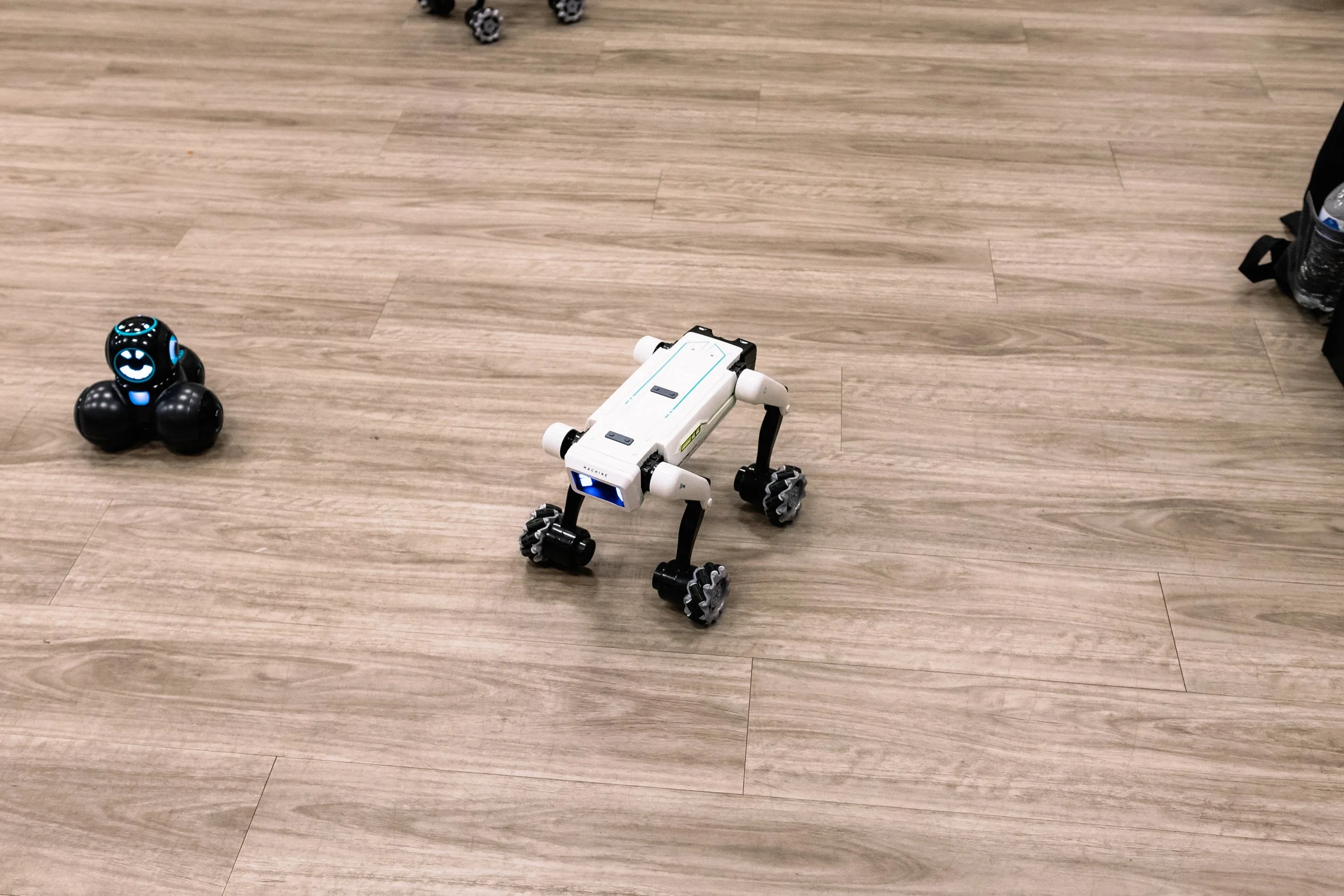 Two small wheeled robots move across the floor during an interactive robotics activity at Chakira’s Cookout.