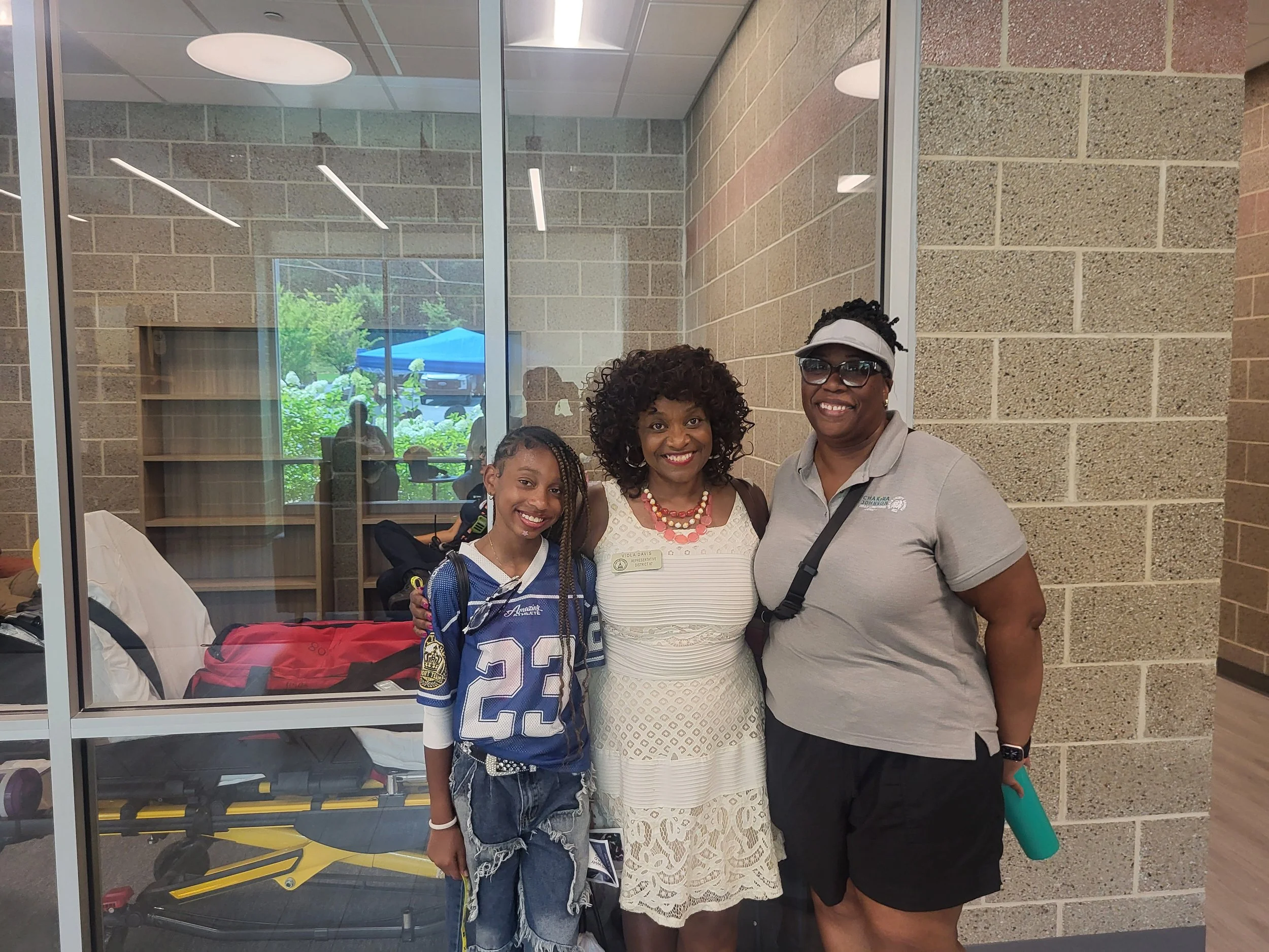 Commissioner Chakira Johnson poses indoors with a smiling young attendee wearing a blue jersey and a woman wearing a white dress.
