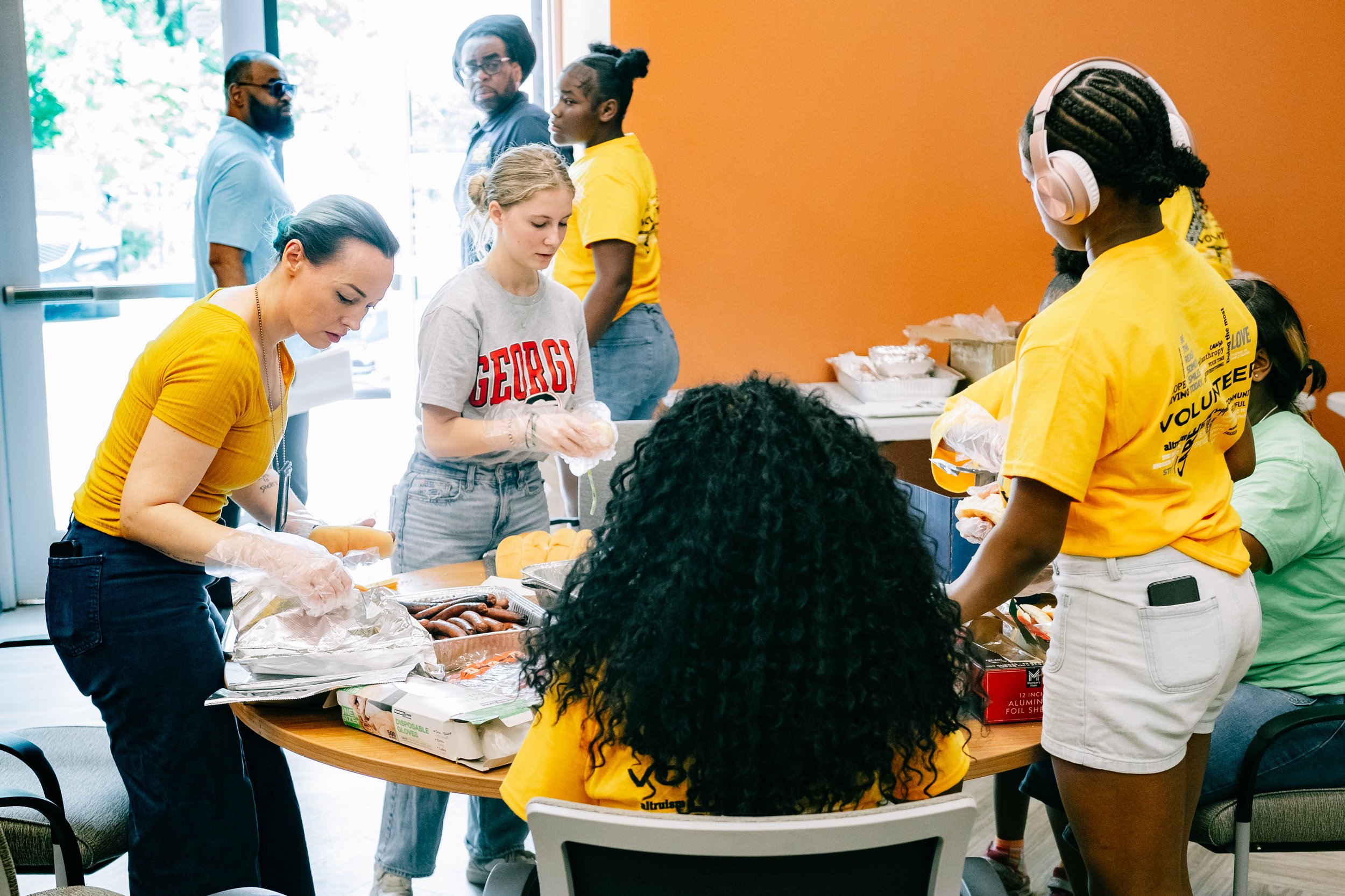 Volunteers form an assembly line to prepare hamburgers and hot dogs for grab-and-go meal bags for guests at Chakira’s Cookout.