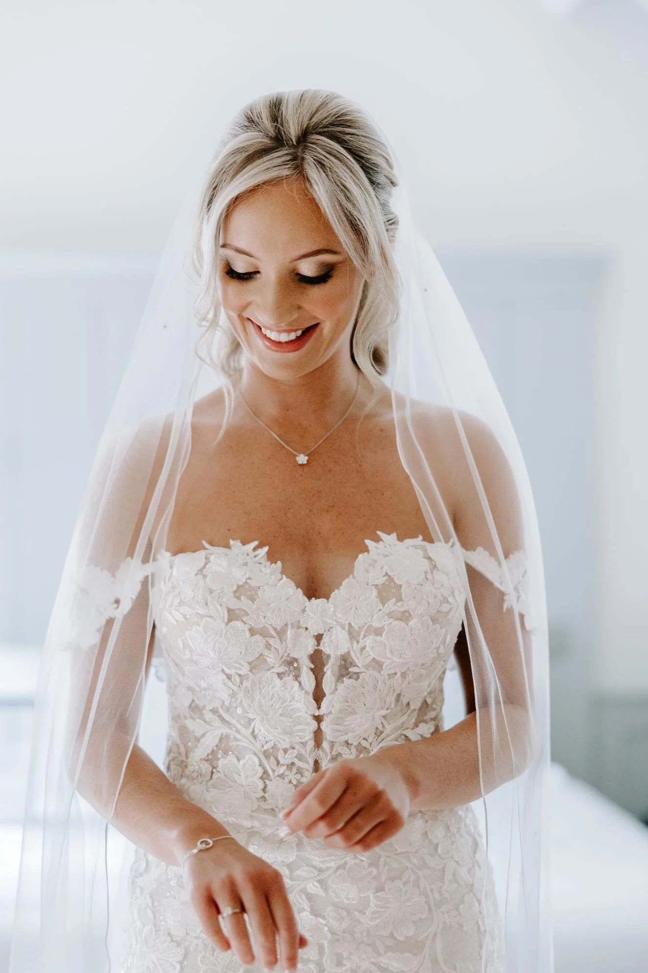Bride in lace wedding dress with veil hair in updo, make up is soft glam