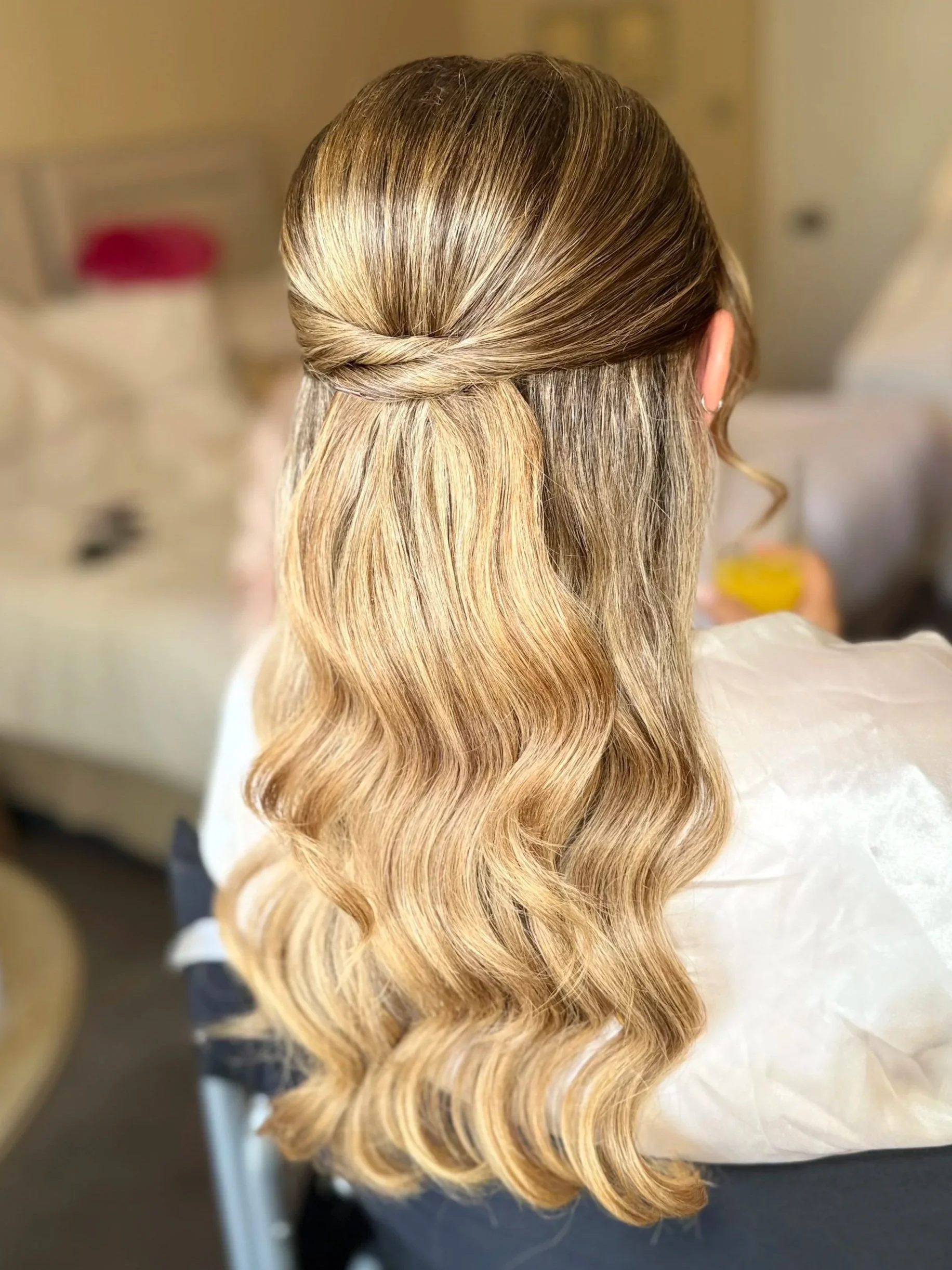 Back view of a woman with long, wavy blonde hair styled with a half-up twist.