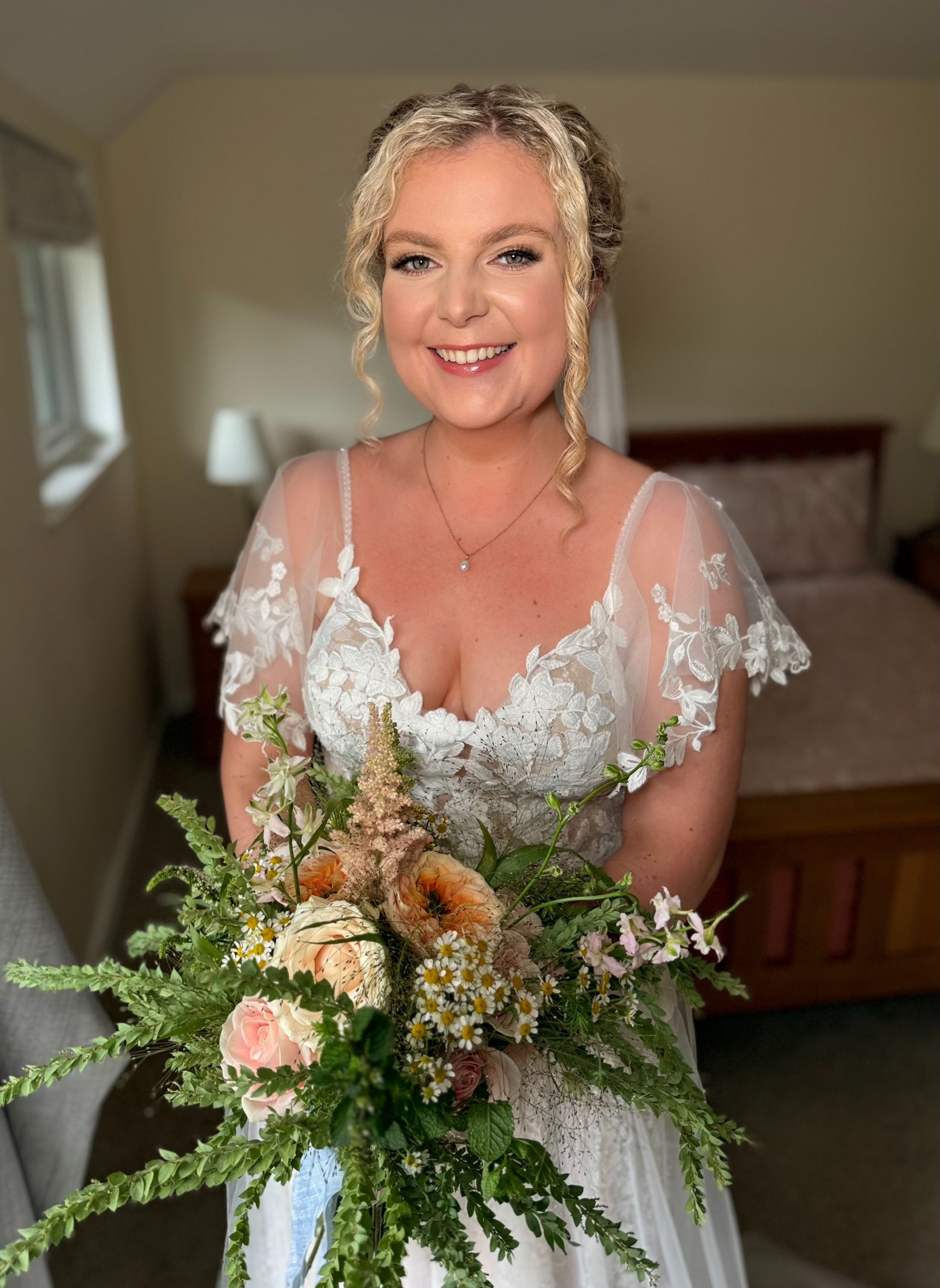 A woman in a wedding dress holding a bouquet of flowers, smiling indoors.