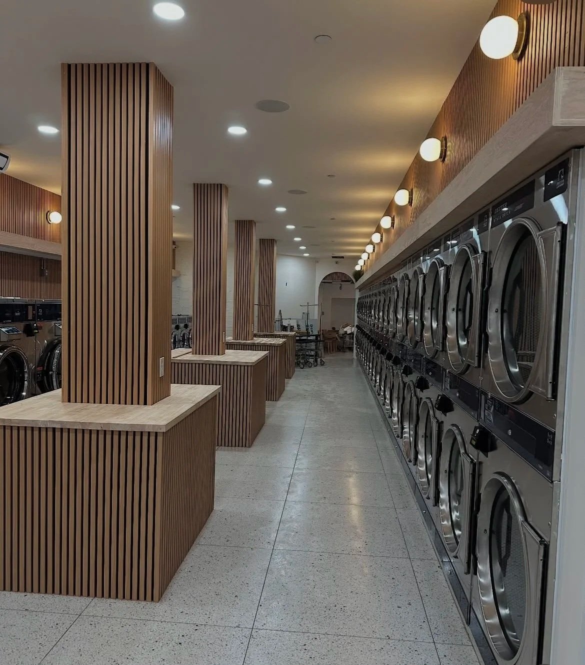 Empty laundromat with wooden pillars and a row of washing machines.