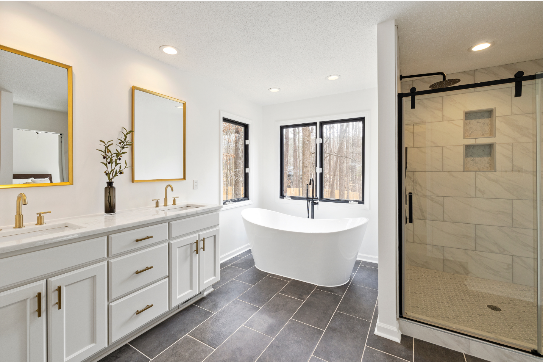 Modern bathroom with double vanity, gold fixtures, large white bathtub, and glass-enclosed shower with marble tiles.