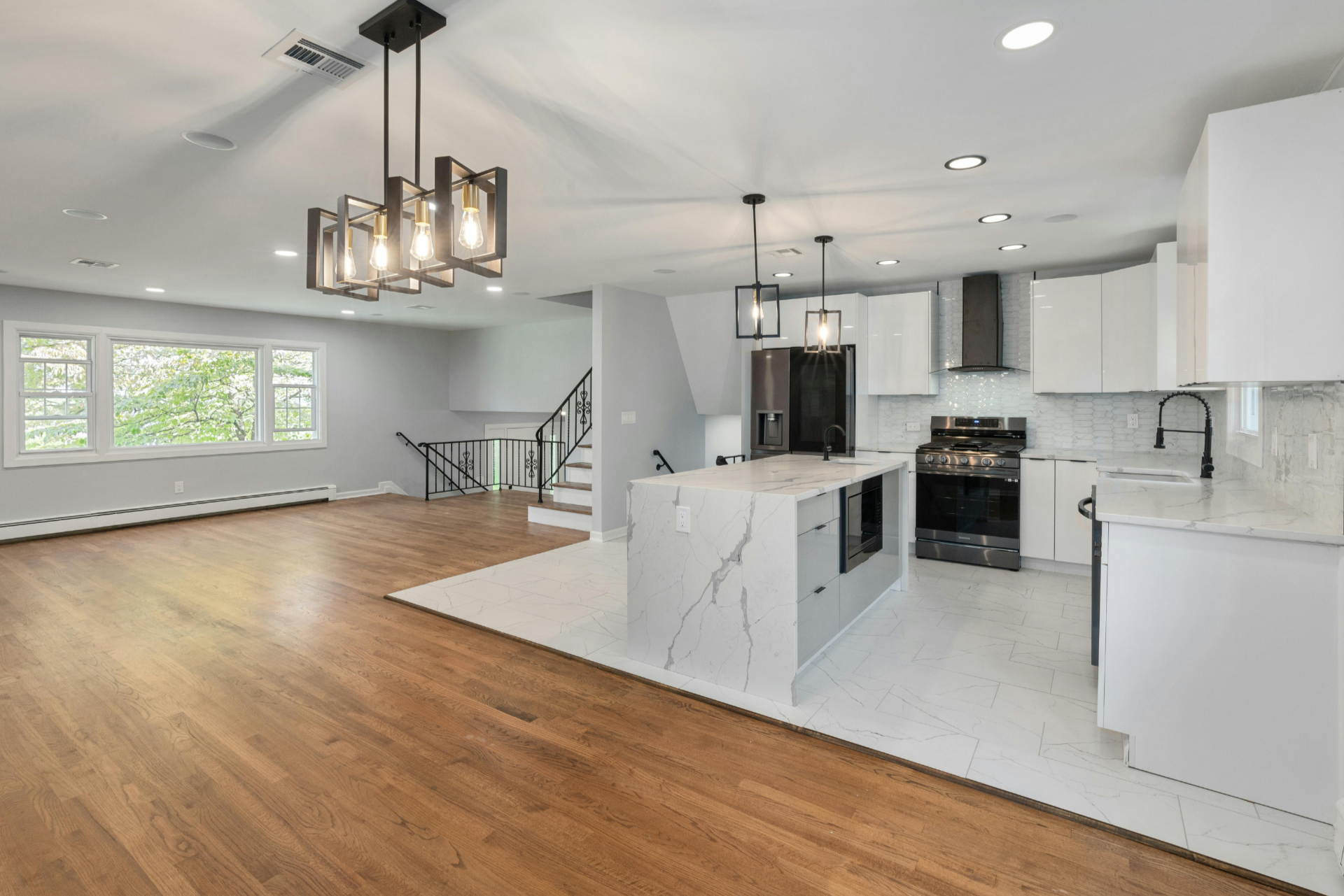 Open-concept living area with kitchen featuring white cabinets, a marble island, black appliances, and hardwood flooring.