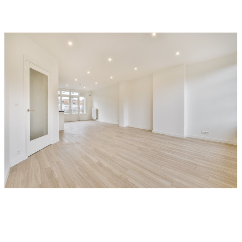 Spacious empty room with wooden floor, white walls, recessed lighting, a closed door, and large windows.