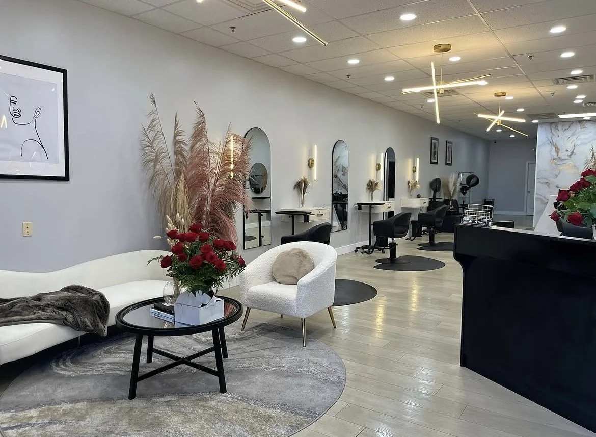 Interior of a modern hair salon with styling stations, large mirrors, styling chairs, and decorative plants.