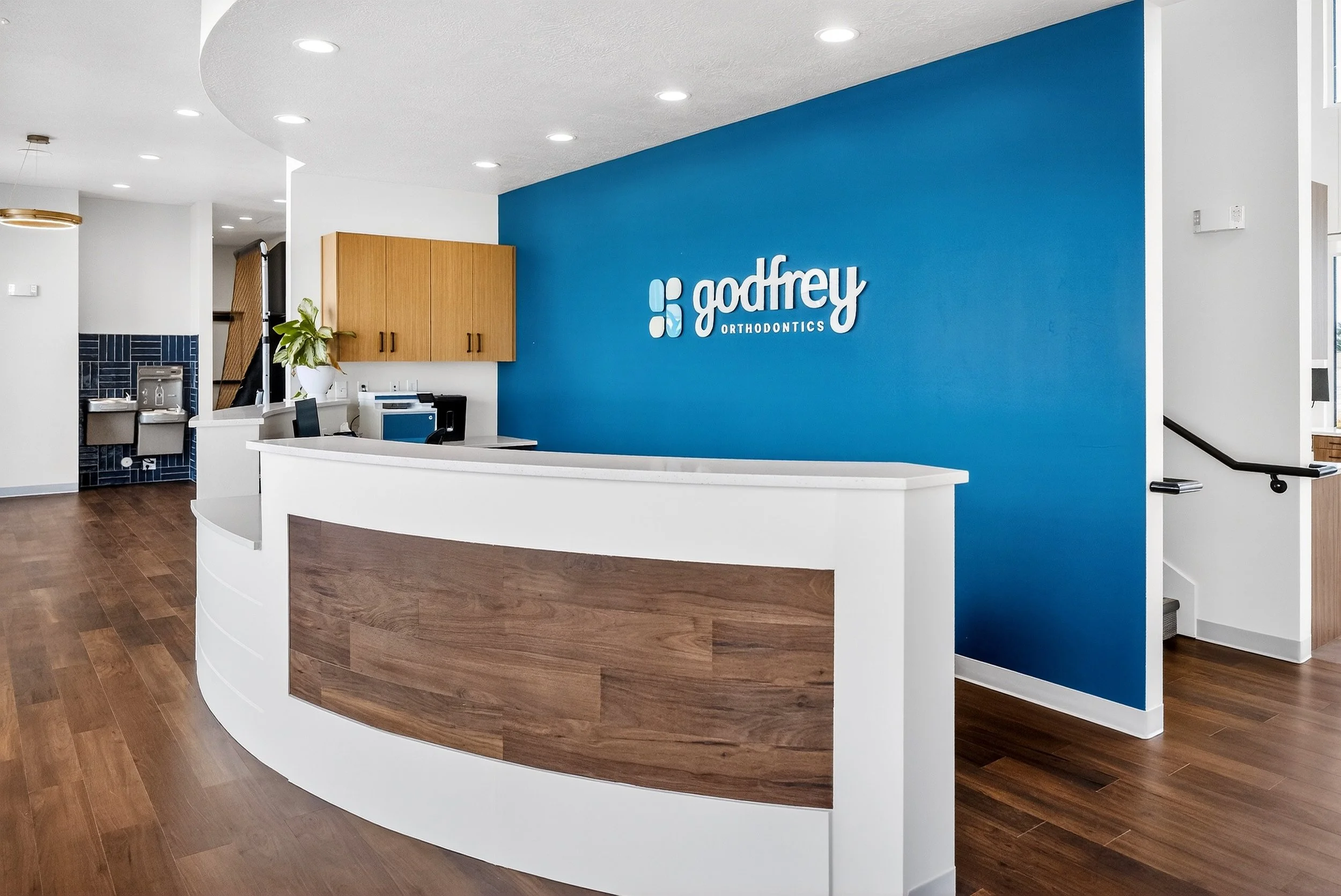 Reception area of Godfrey Orthodontics with a white curved desk, wooden accents, a blue accent wall with the company's logo.