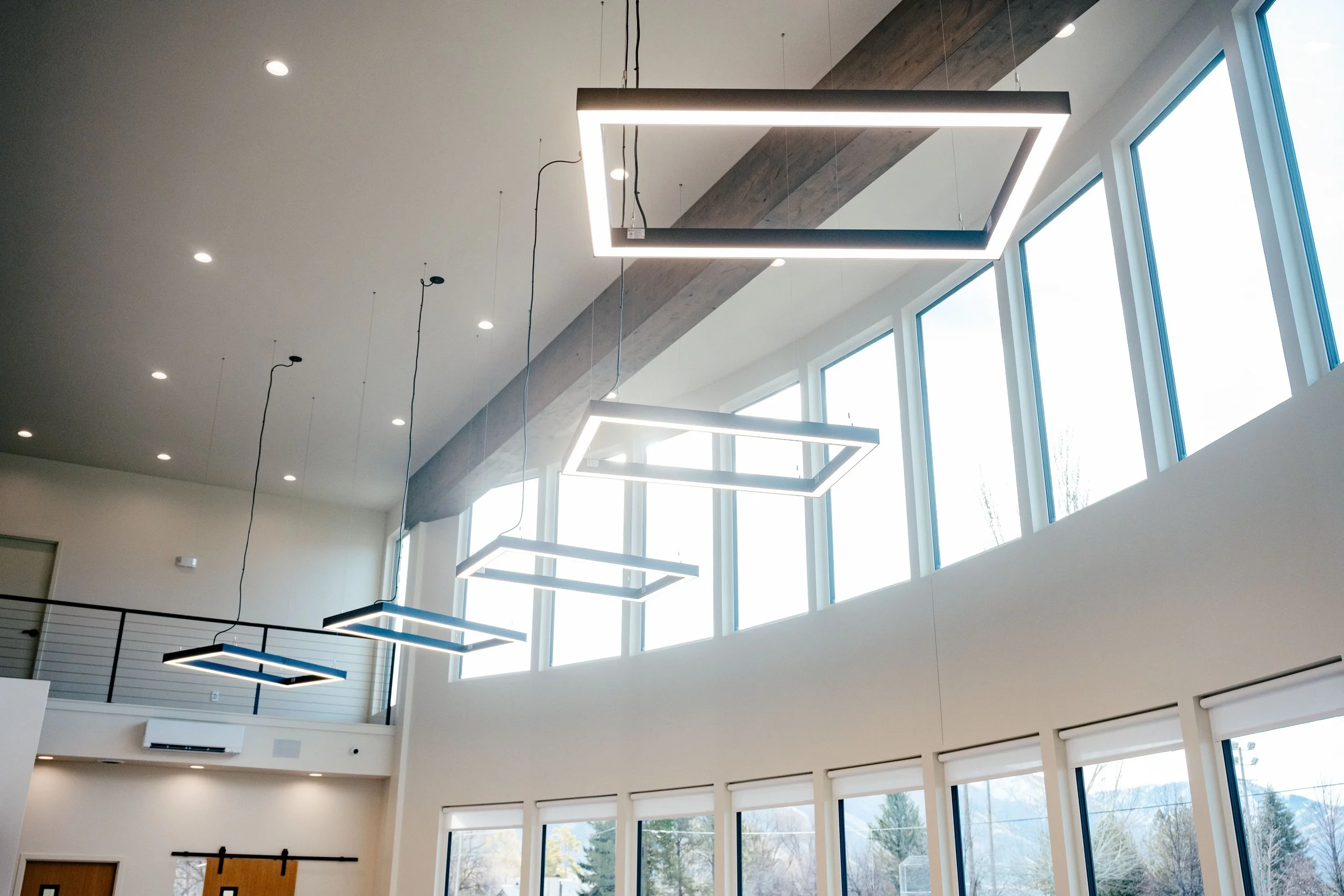 Interior of a modern building with high ceilings, large windows, and rectangular pendant lights hanging from the ceiling.
