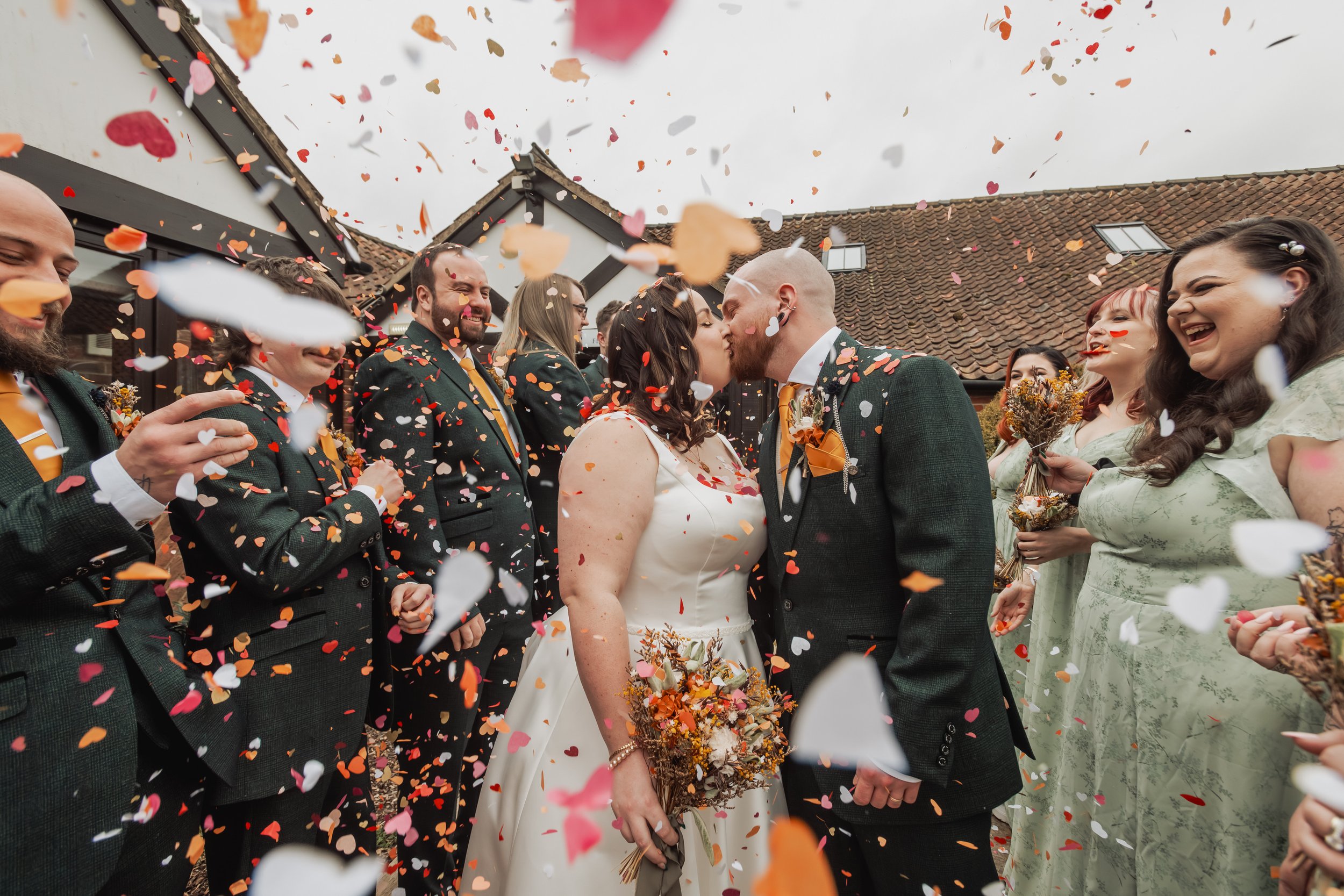 Bride and groom kissing while wedding guests throw confetti around them