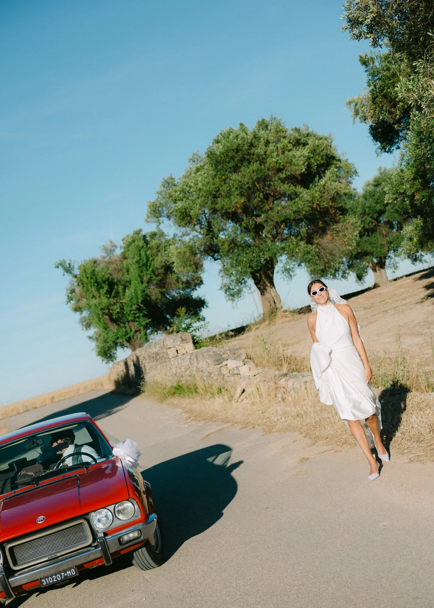 Bride and groom with a vintage red car in italian landscape