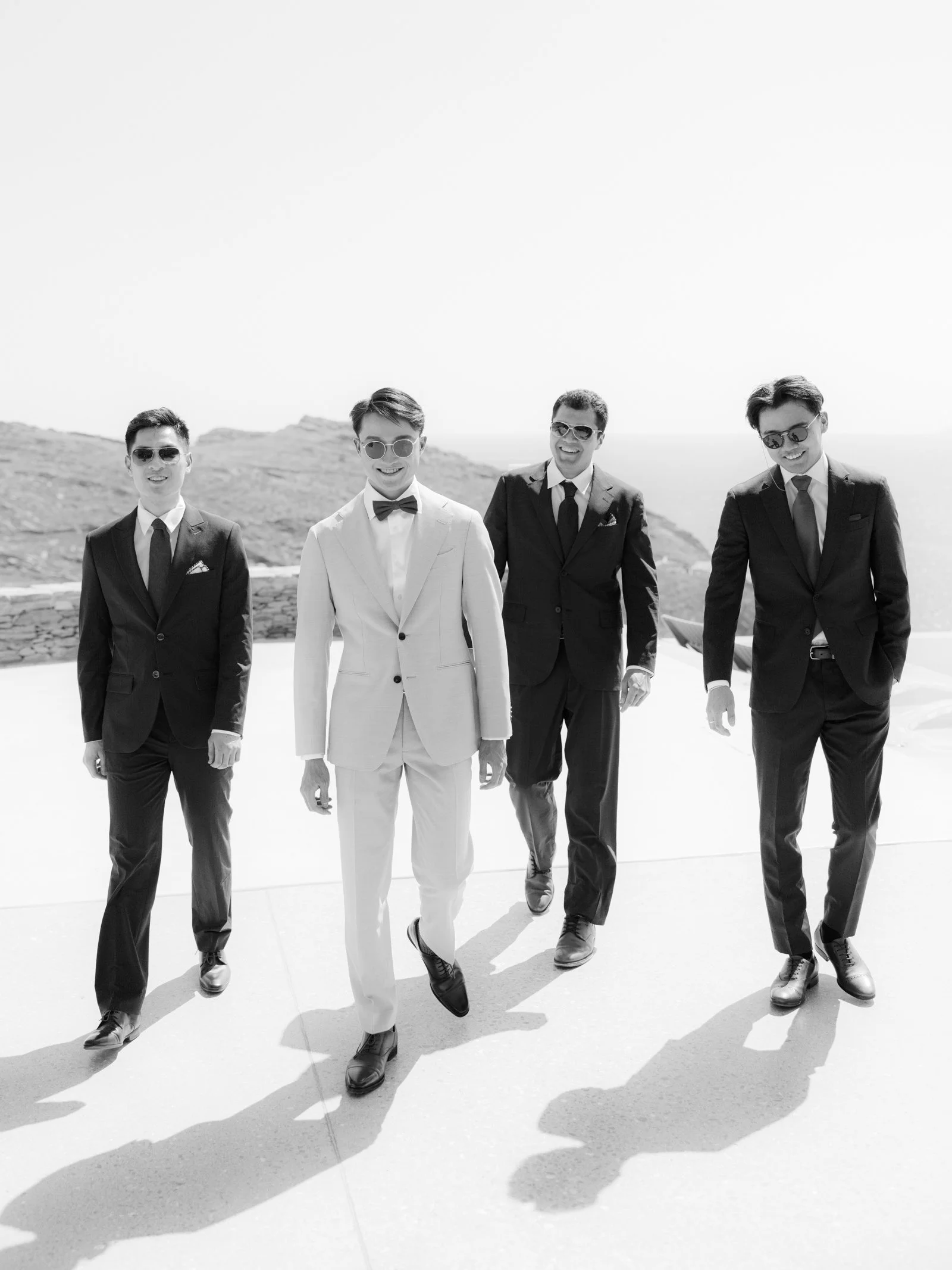 Groom an 3 best men walking toward the camera all wearing suits.