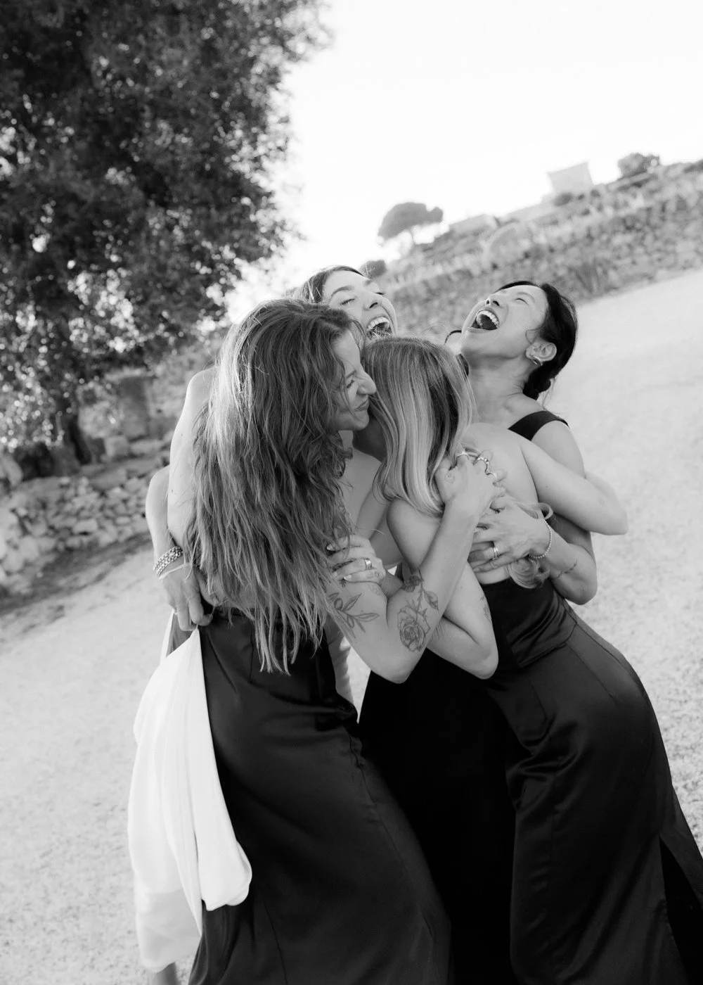 Group of women embracing and laughing outdoors, black and white photo.