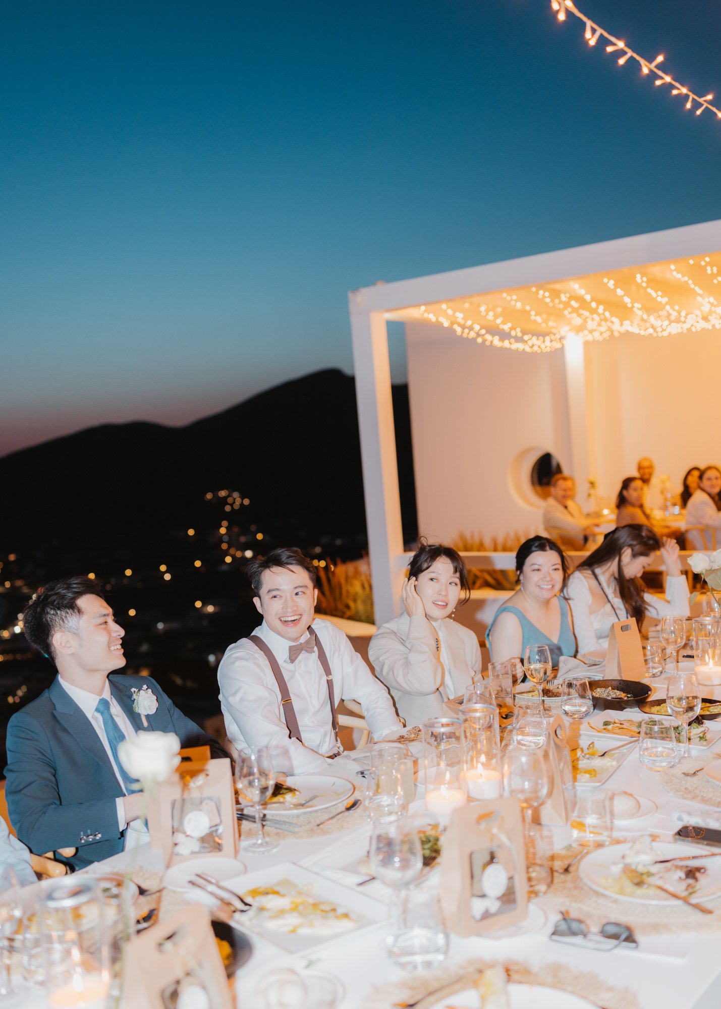 Wedding crowd at a dinner talble under the open sky after sunset.