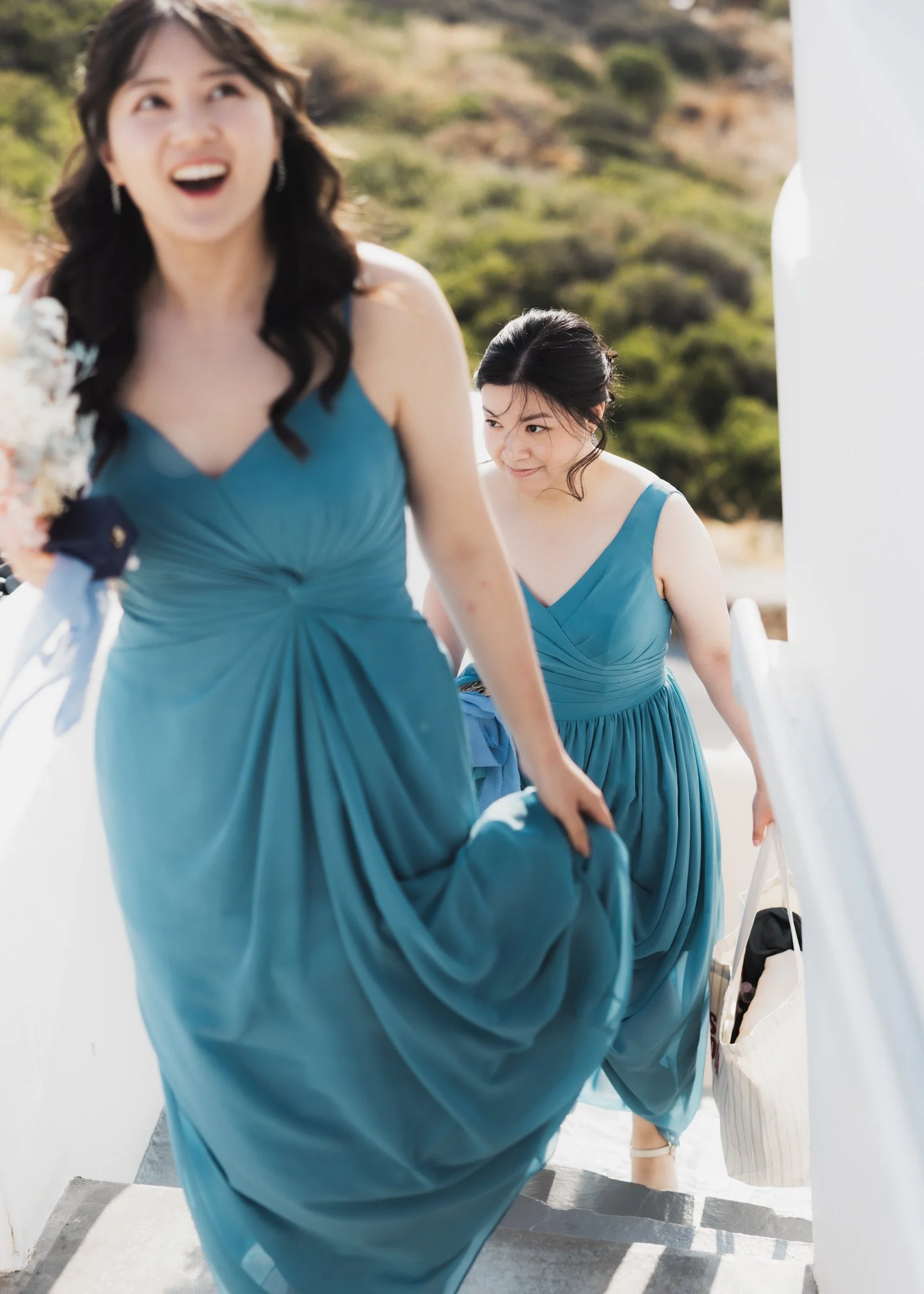 Two bridesmaids in blue dresses walking up some stairs outside.