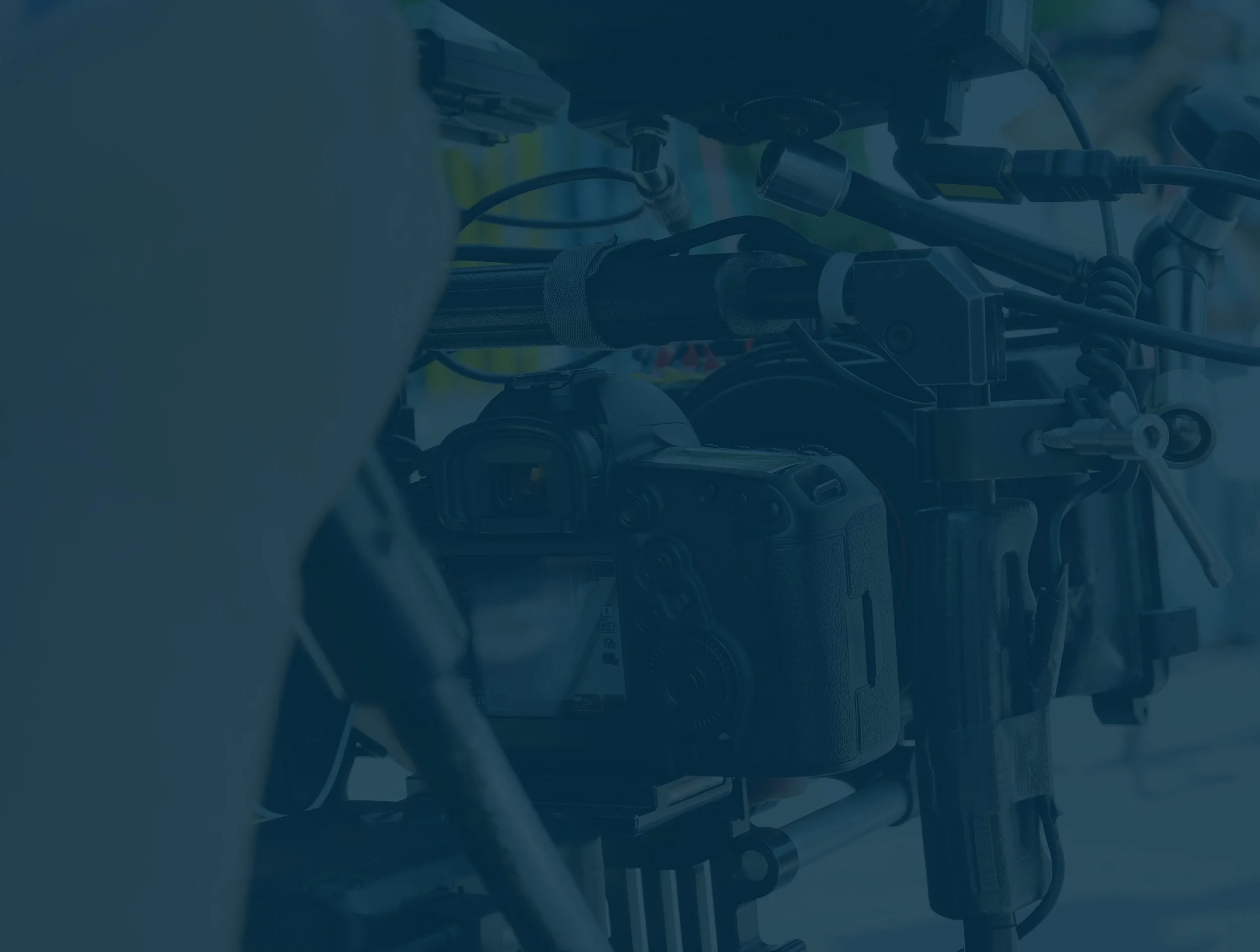 Close-up of a professional camera mounted on film or video equipment, with cables and mechanical parts visible.