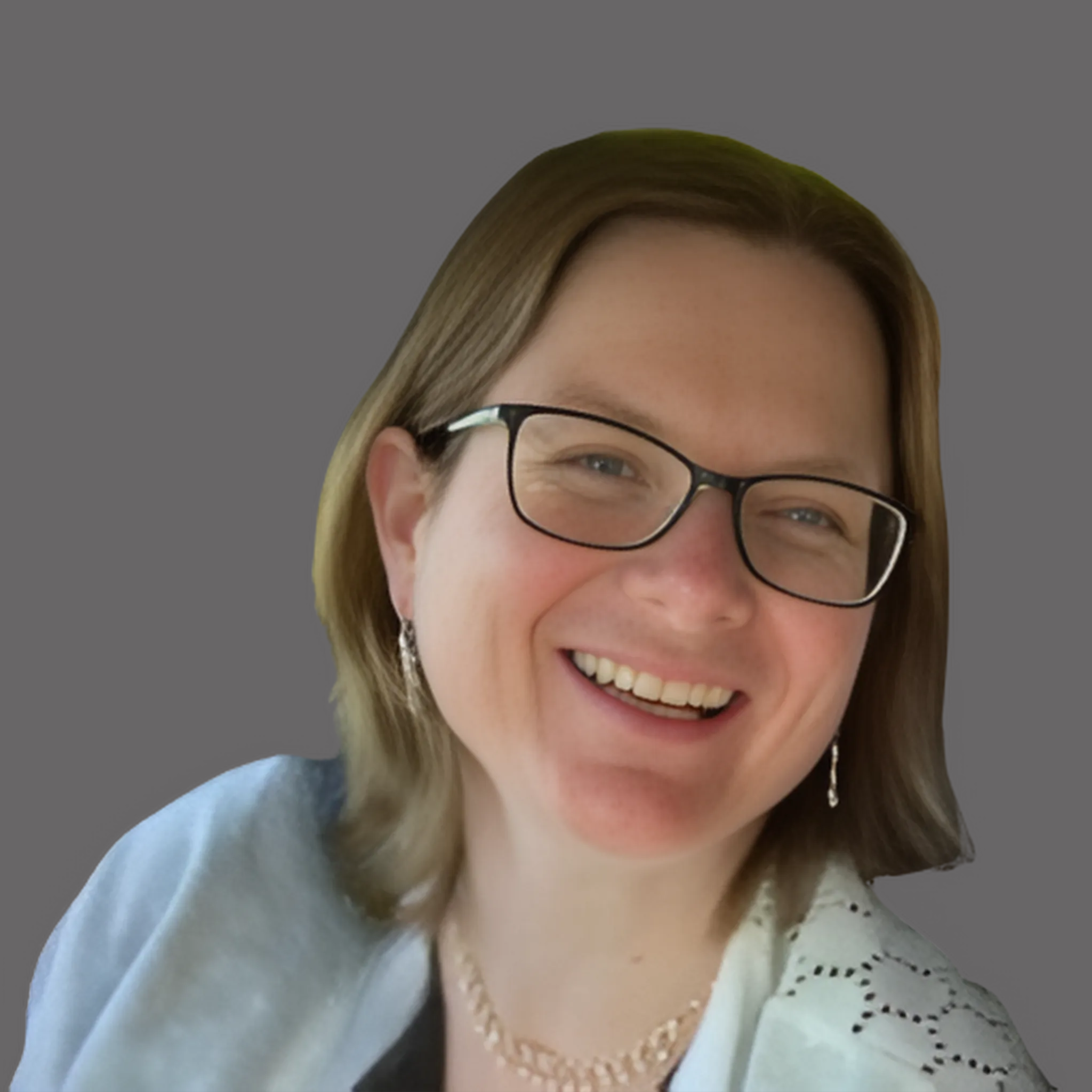 A woman smiling with shoulder-length brown hair, wearing glasses, earrings, a light blue jacket, and a necklace, against a gray background.