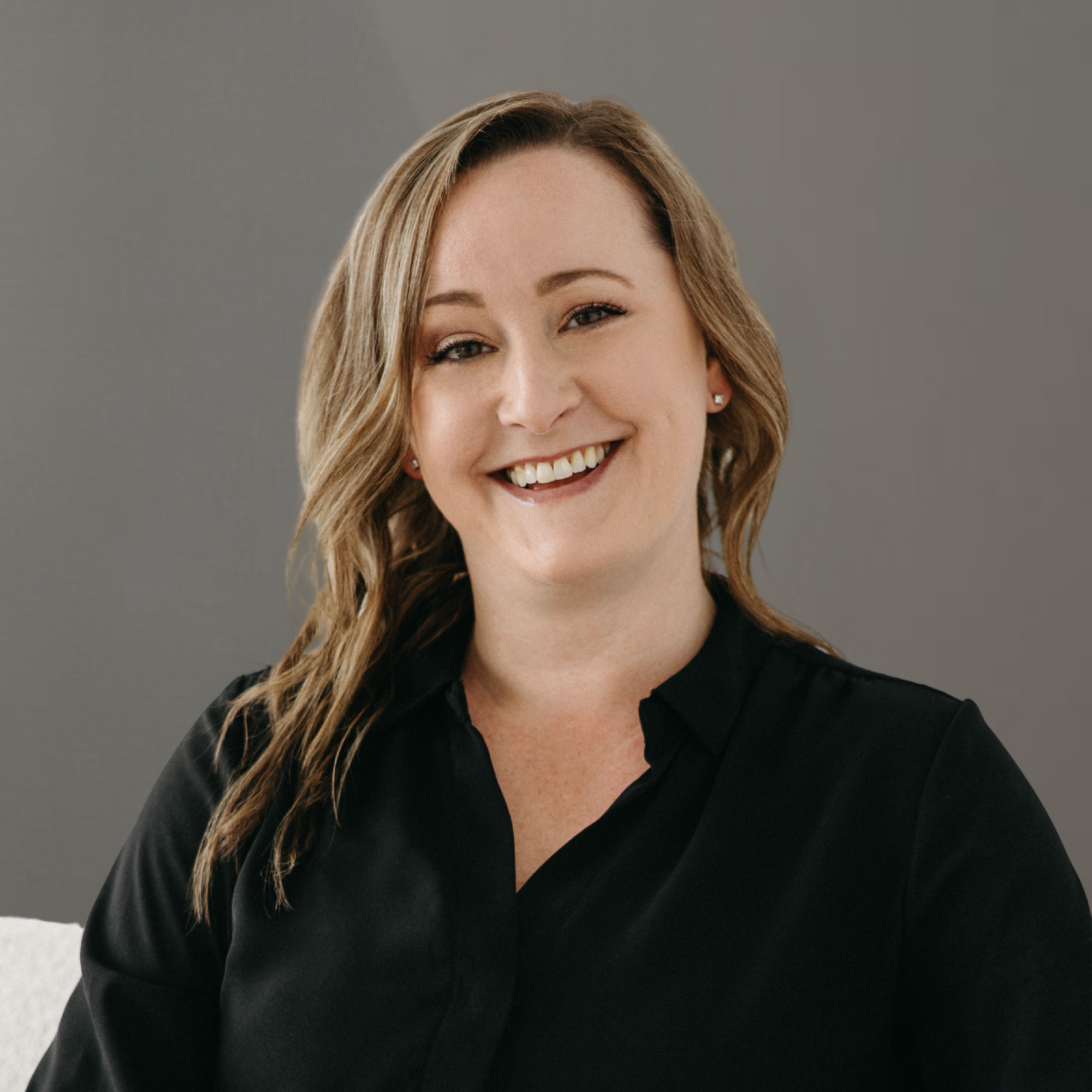 A woman with shoulder-length wavy blonde hair smiling, wearing a black blouse against a gray background.
