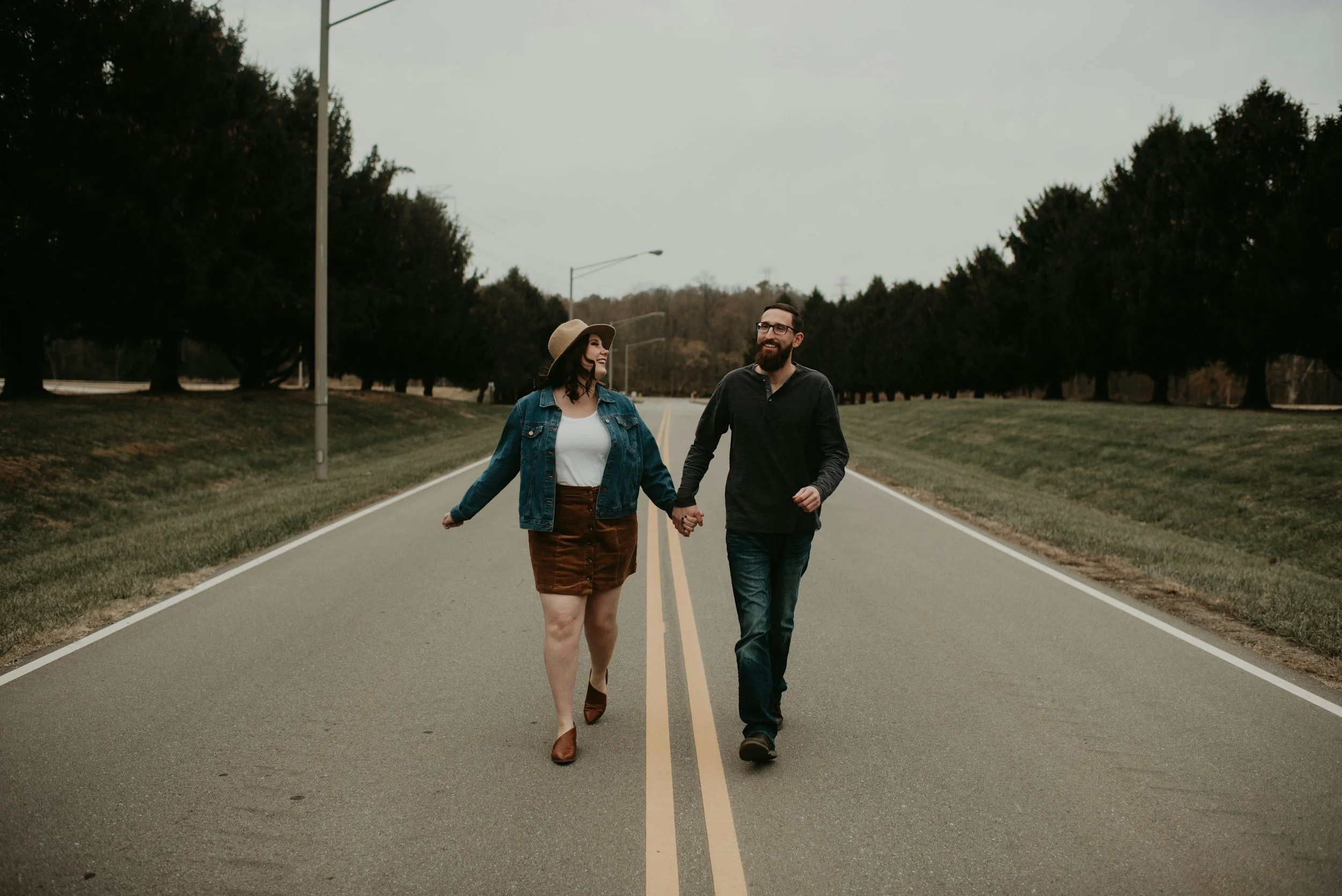 A couple walking hand-in-hand on a quiet rural road with trees in the background.