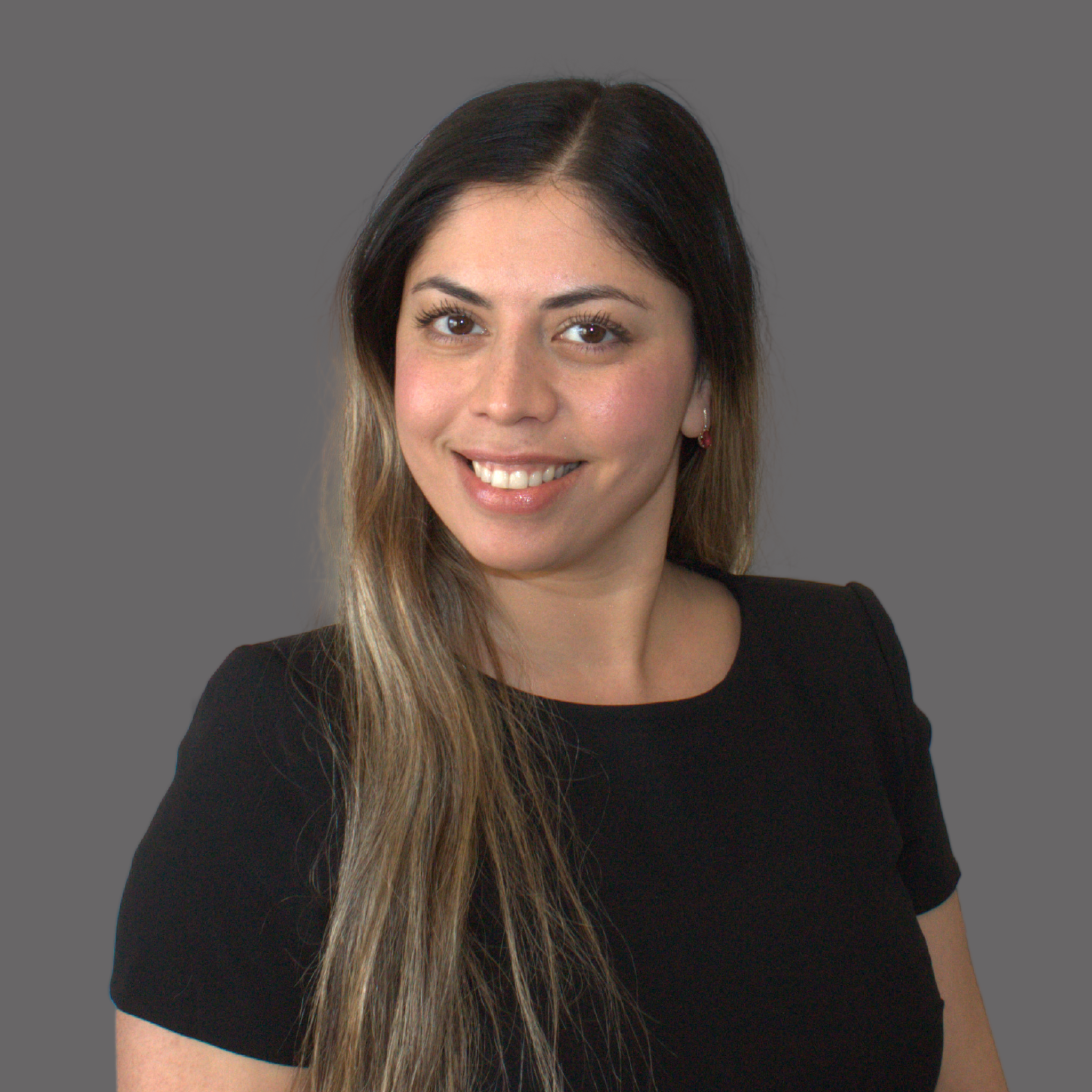 A smiling woman with long brown hair, wearing a black top, standing against a gray background.