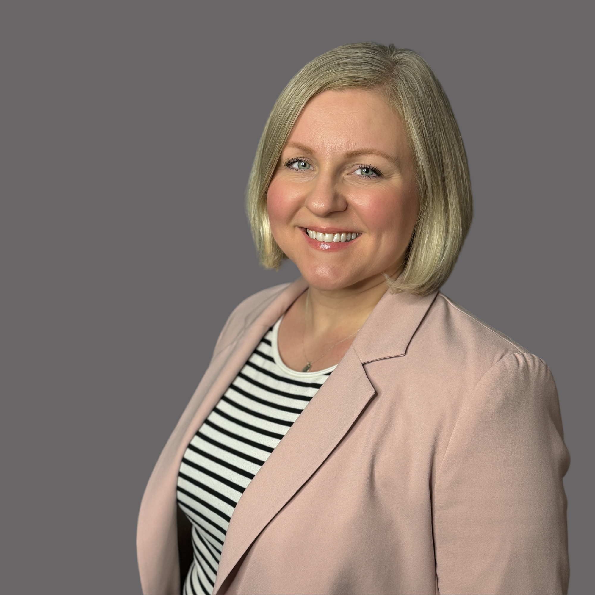 A woman with blonde hair, wearing a beige blazer over a black and white striped shirt, smiling at the camera against a gray background.
