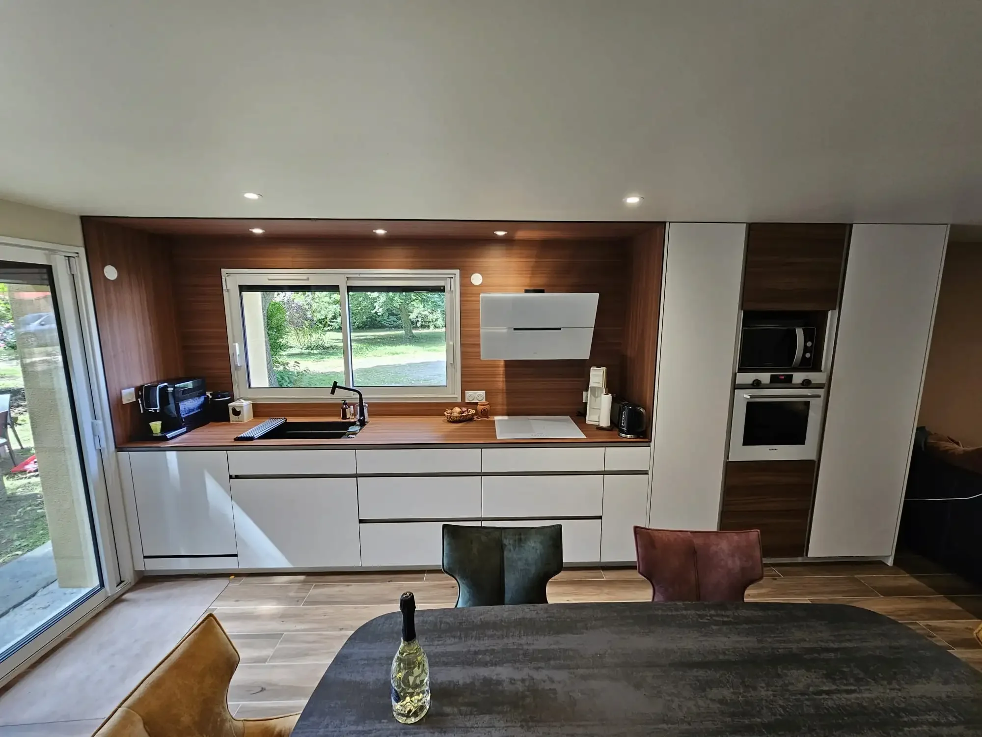 Cuisine contemporaine en bois et blanc avec ligne épurée et vue sur jardin, conçue sur mesure par Oleksiak à Clermont-Ferrand.