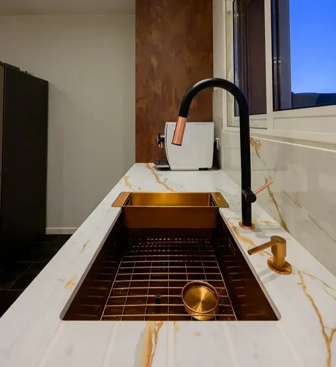 Détail d’un évier en laiton avec robinet noir et plan de travail en pierre dans une cuisine sur mesure contemporaine à Clermont-Ferrand.