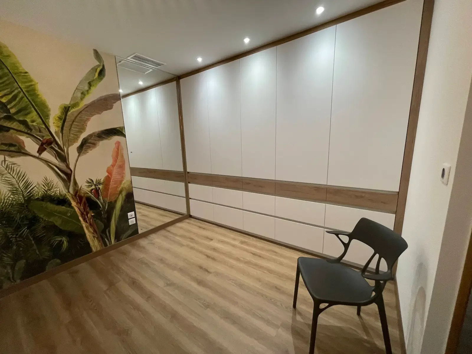 Dressing contemporain conçu par Oleksiak à Clermont-Ferrand, avec façades blanches, inserts en bois naturel, éclairage intégré et miroir pleine hauteur, créant un espace fonctionnel et élégant.