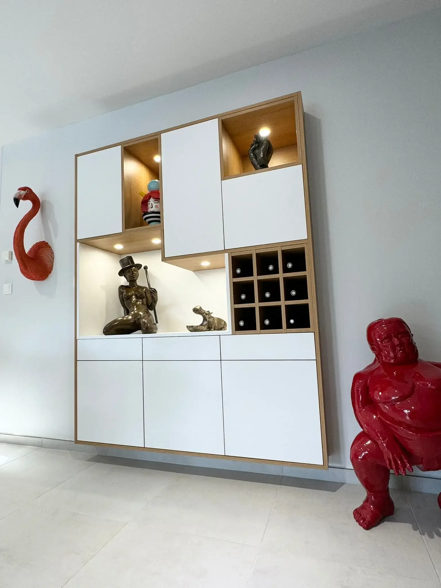 Meuble de rangement suspendu blanc et bois conçu sur mesure par Oleksiak à Clermont-Ferrand, combinant niches décoratives, casier à bouteilles et éclairage intégré.