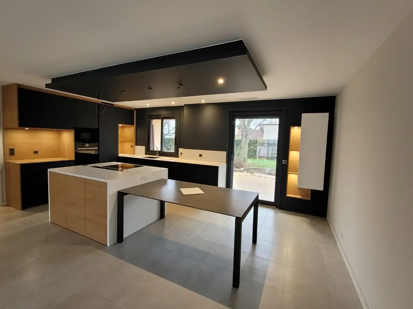 Cuisine moderne noire et bois avec îlot central et coin repas intégré, réalisée sur mesure par Oleksiak à Clermont-Ferrand.