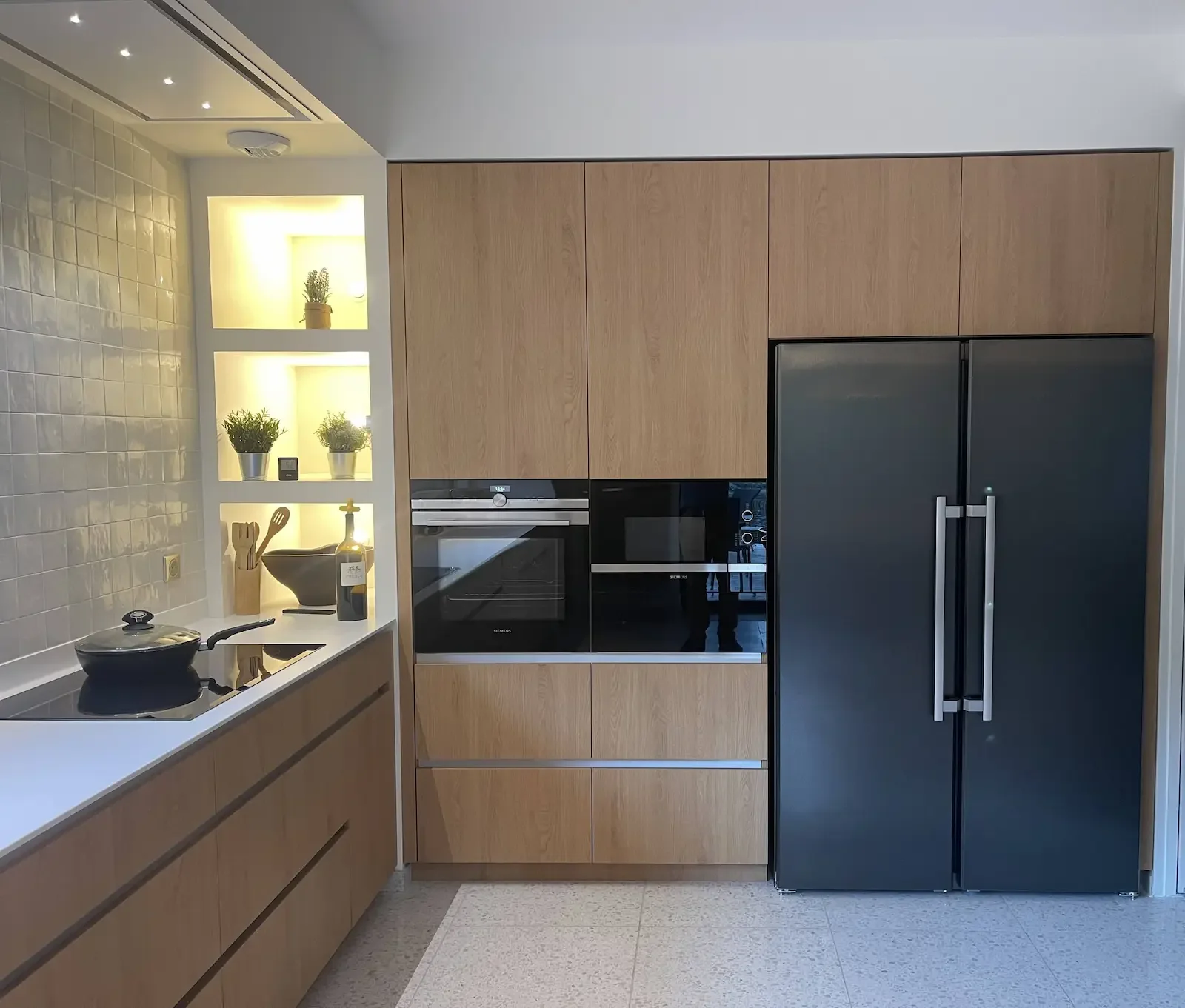 Cuisine sur mesure réalisée par Oleksiak à Clermont-Ferrand, alliant façades en bois clair, électroménagers noirs encastrés et niches lumineuses, pour un design contemporain et chaleureux.