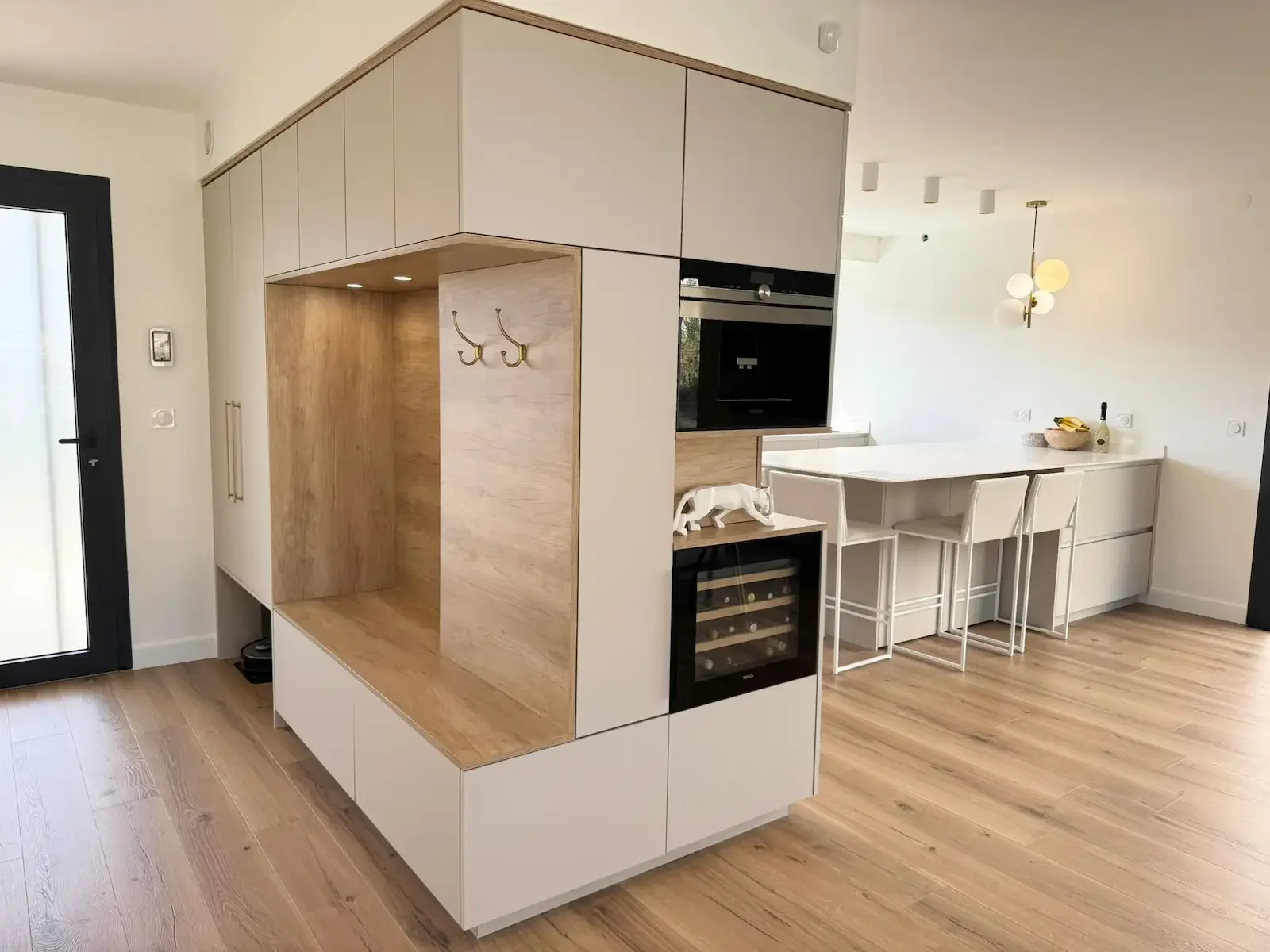 Ilot multifonction alliant cuisine et entrée, réalisé en finition cachemire et bois clair par Oleksiak à Clermont-Ferrand. Un aménagement sur mesure combinant assise, rangements et cave à vin intégrée.