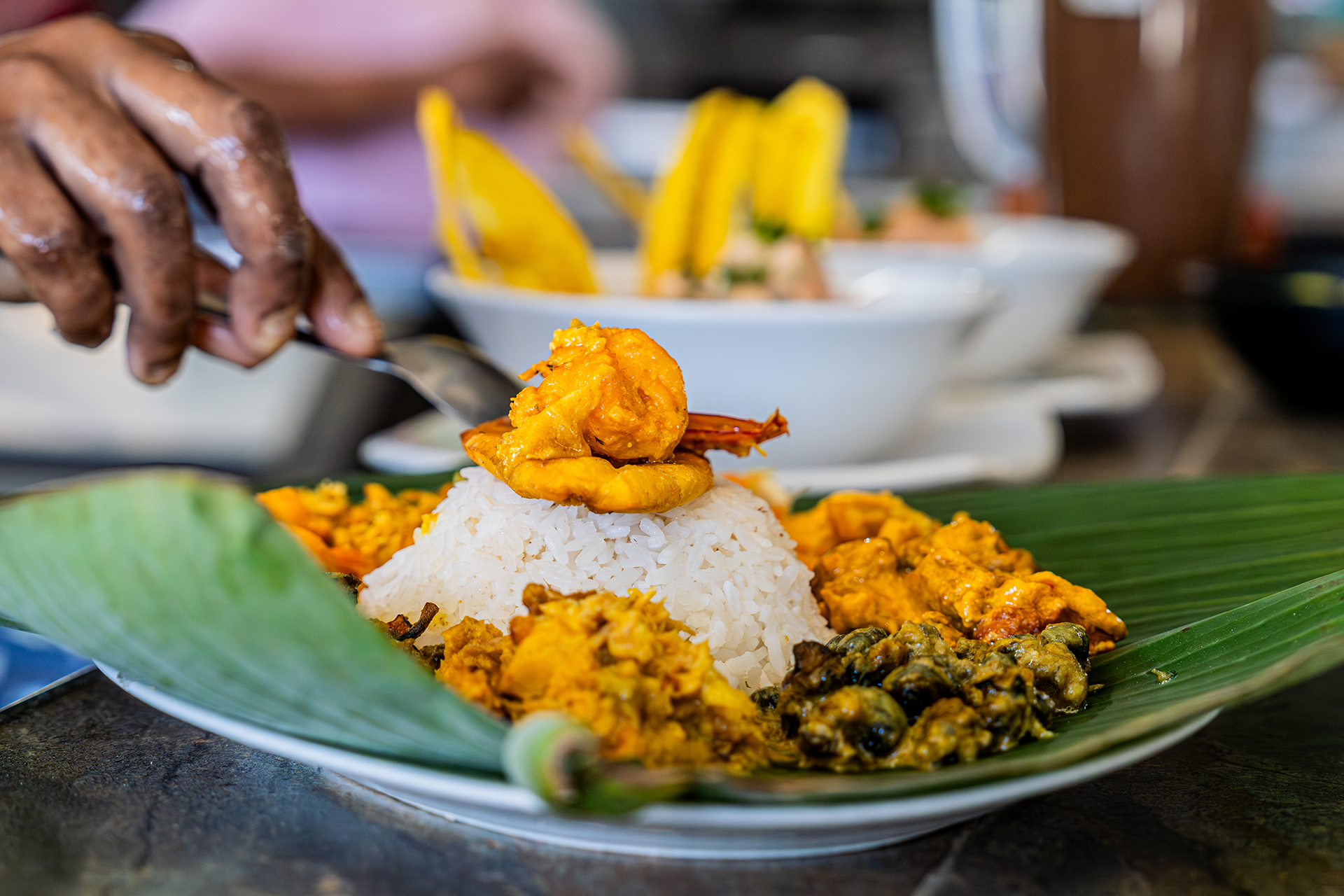 Plato de arroz blanco con camarón frito en la parte superior, acompañado de variedad de currys y guisos con legumbres, todo sobre una hoja de plátano.