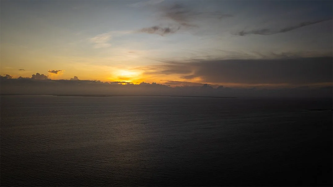 Atardecer sobre el océano con nubes en el cielo y la superficie del agua en calma.